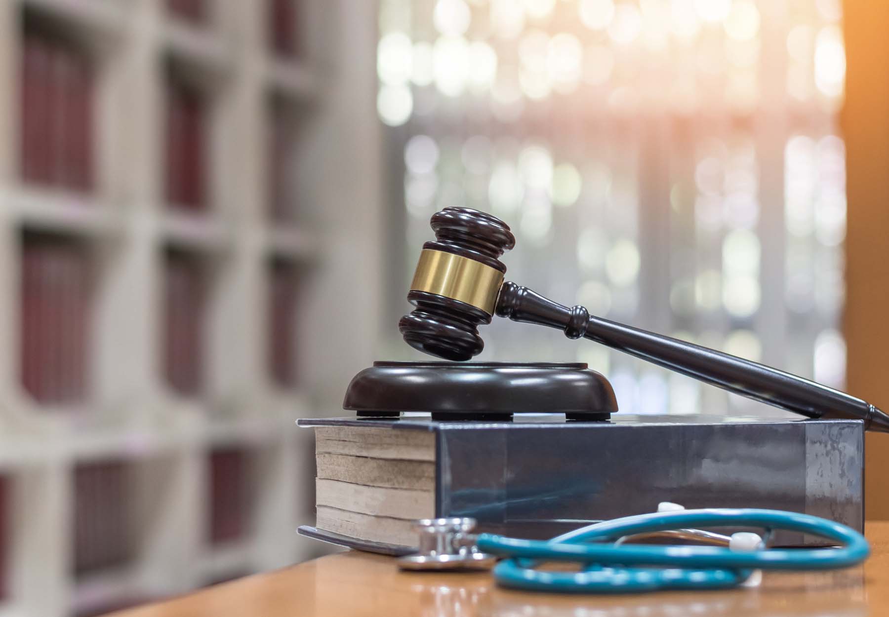 A gavel rests on a large book next to a stethoscope to illustrate court cases involving labs and pathology practices