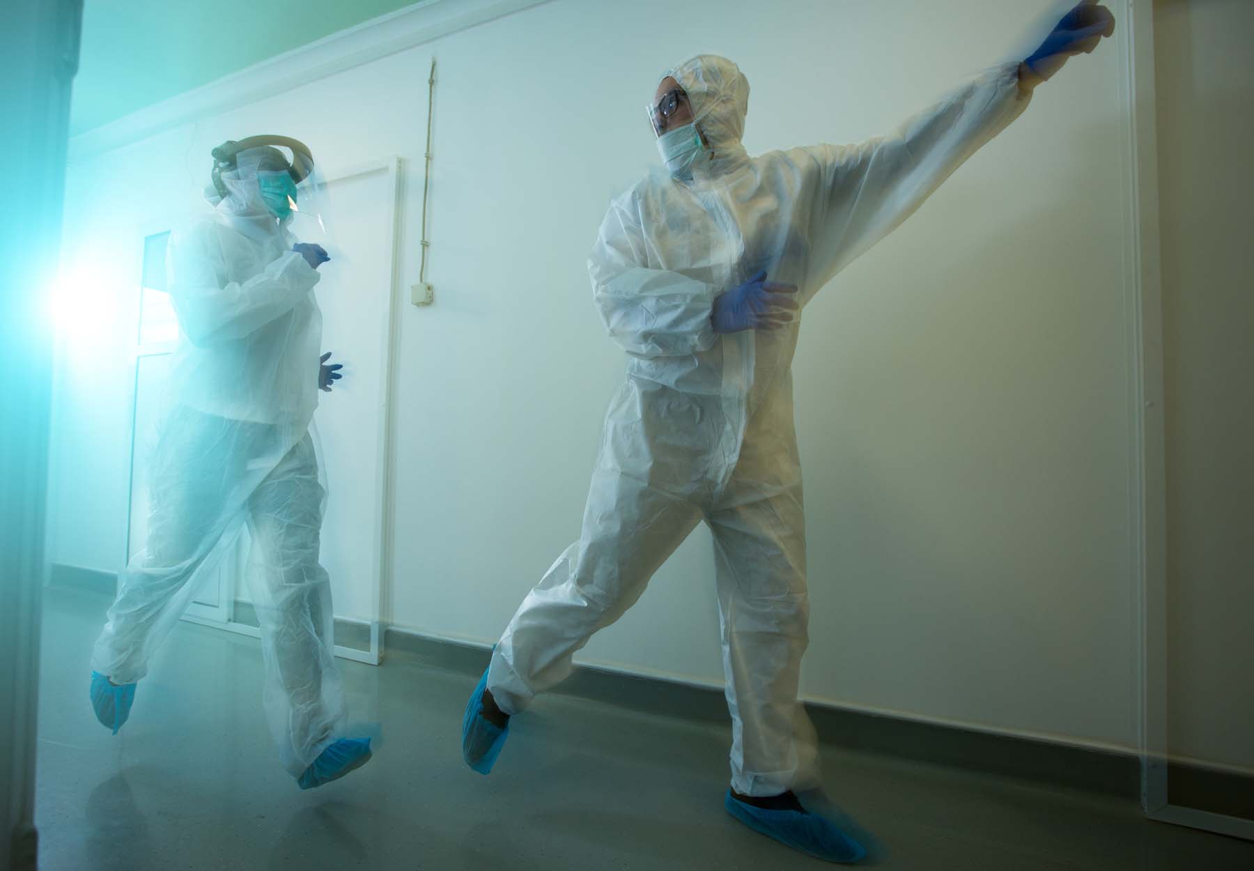 Biosafety lab employees in full PPE are running down a hallway away from a lab accident