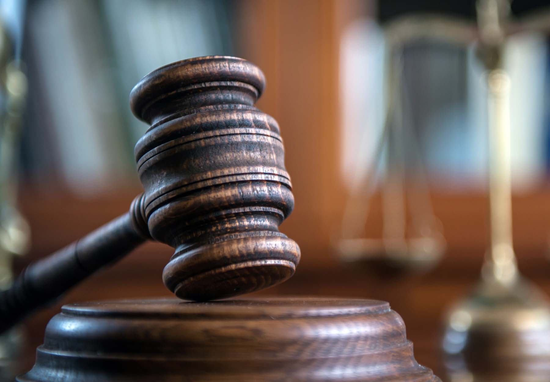 A judge's gavel on a desk with scales in the background to illustrate justice.