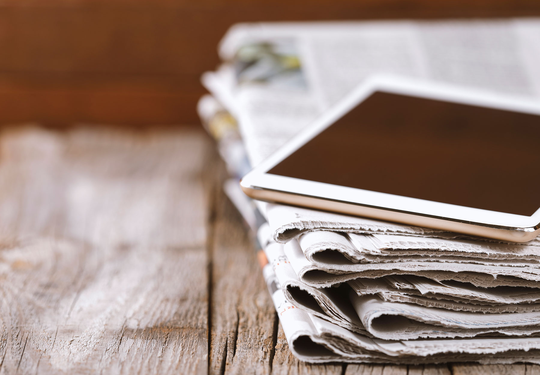 A tablet sitting on top of a stack of newspapers to illustrate the concept of digital news.