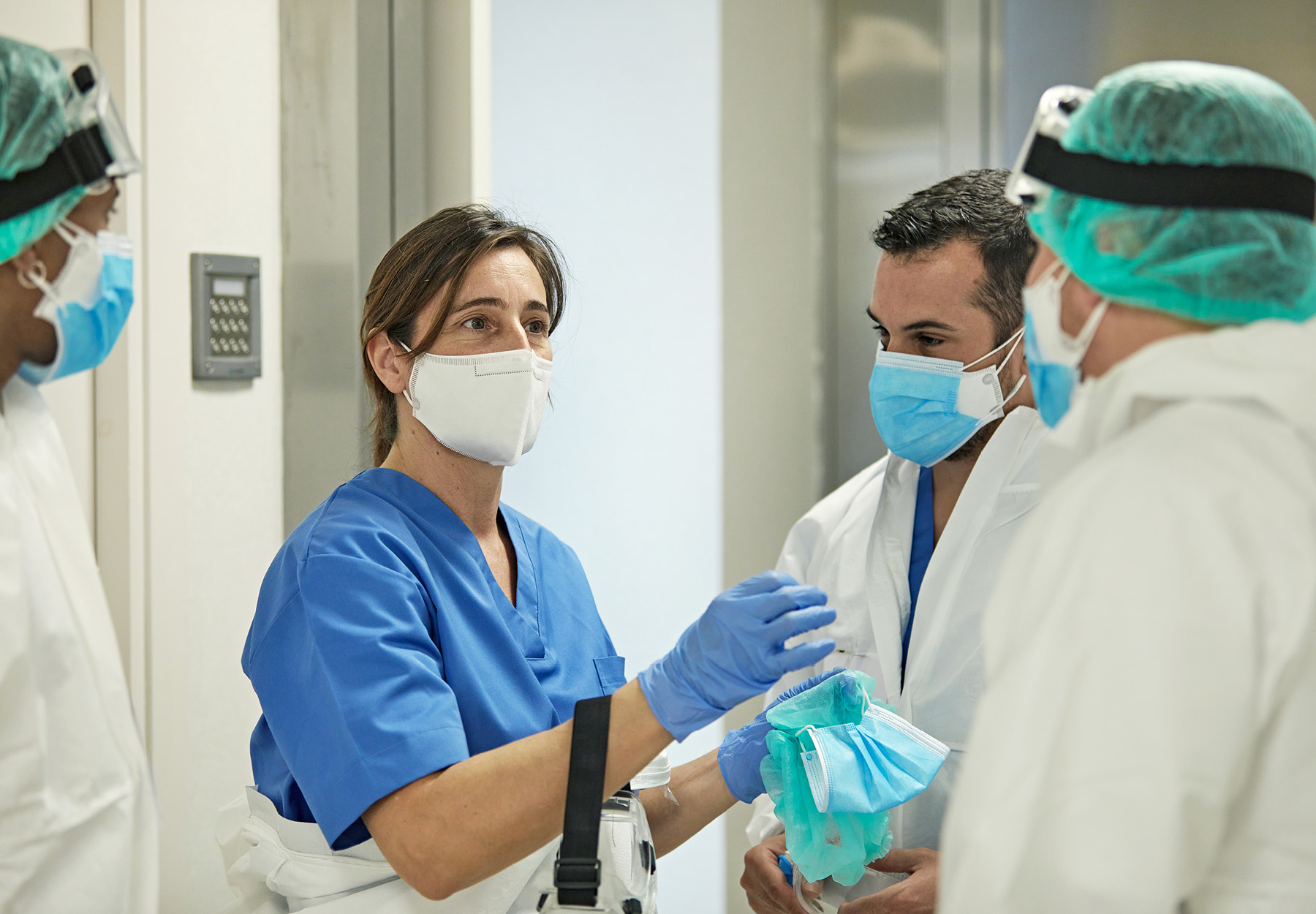 Health care workers wearing PPE meet in a hallway.