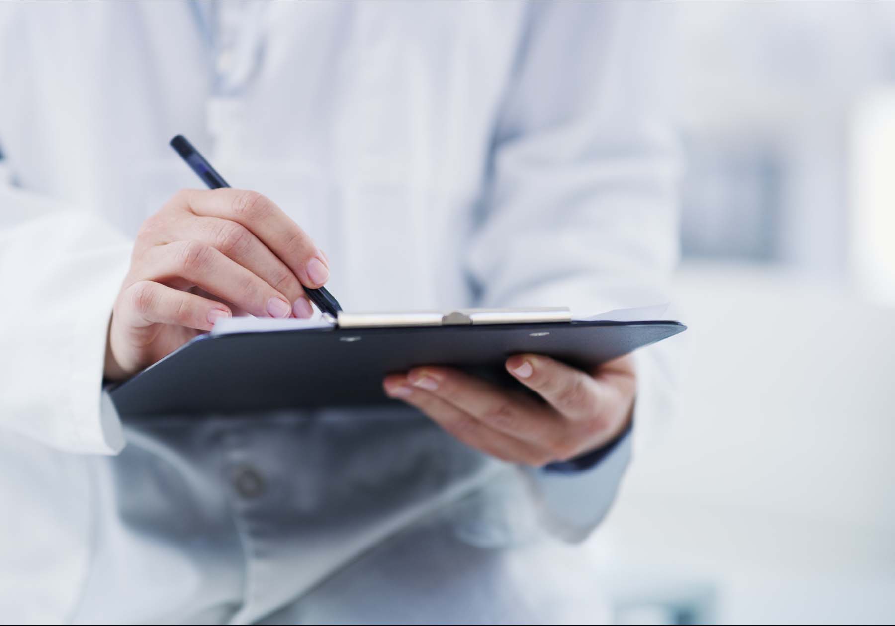 Someone wearing a lab coat is filling out a clipboard in the lab.