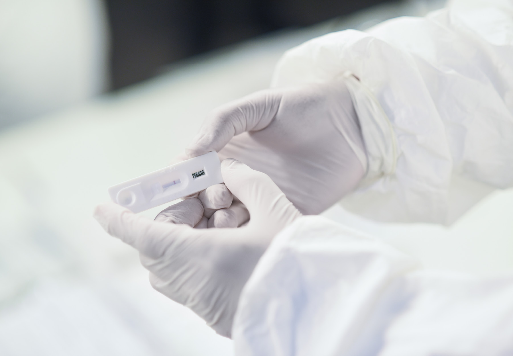 A closeup of a medical professional in full PPE holding an in vitro diagnostic test cartridge.