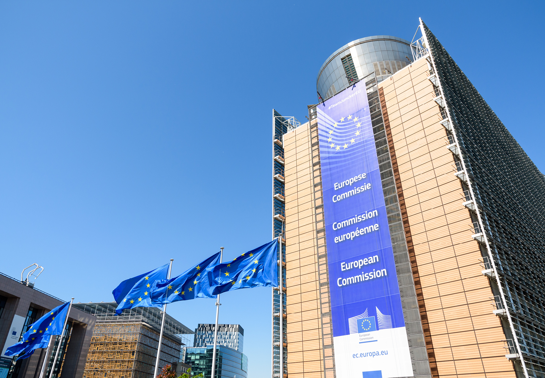 An image of the European Commission (EC) building with three EC flags in front.