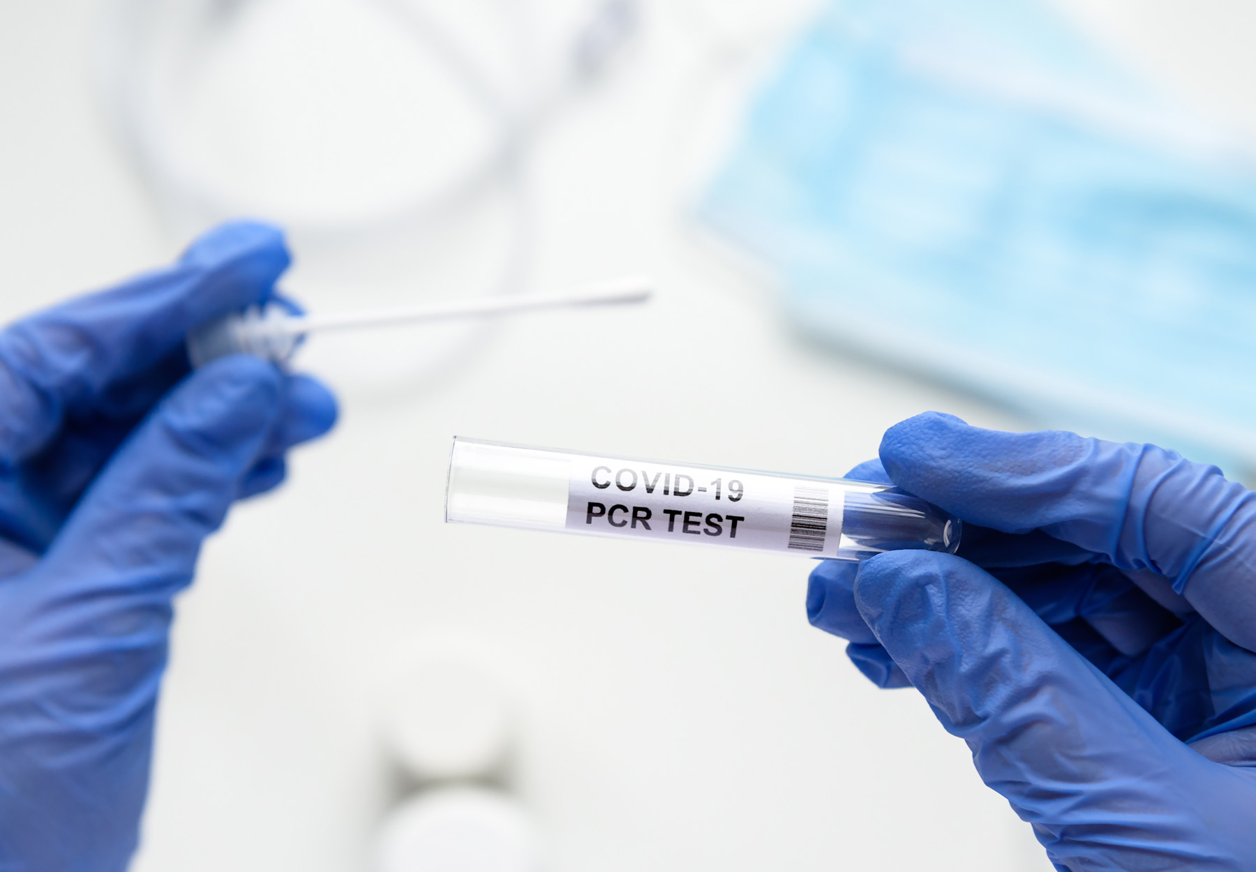 A closeup of gloved hands of a lab tech holding a COVID-19 PCR test vial