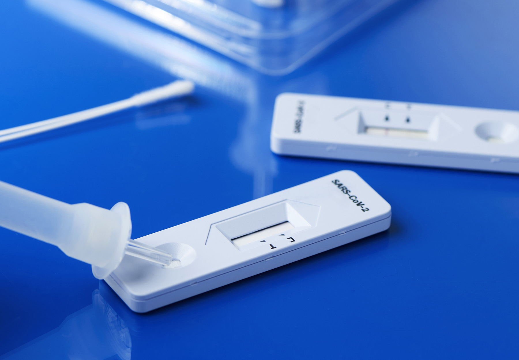 An image of SARS-CoV-2 rapid tests and associated materials on a blue background.