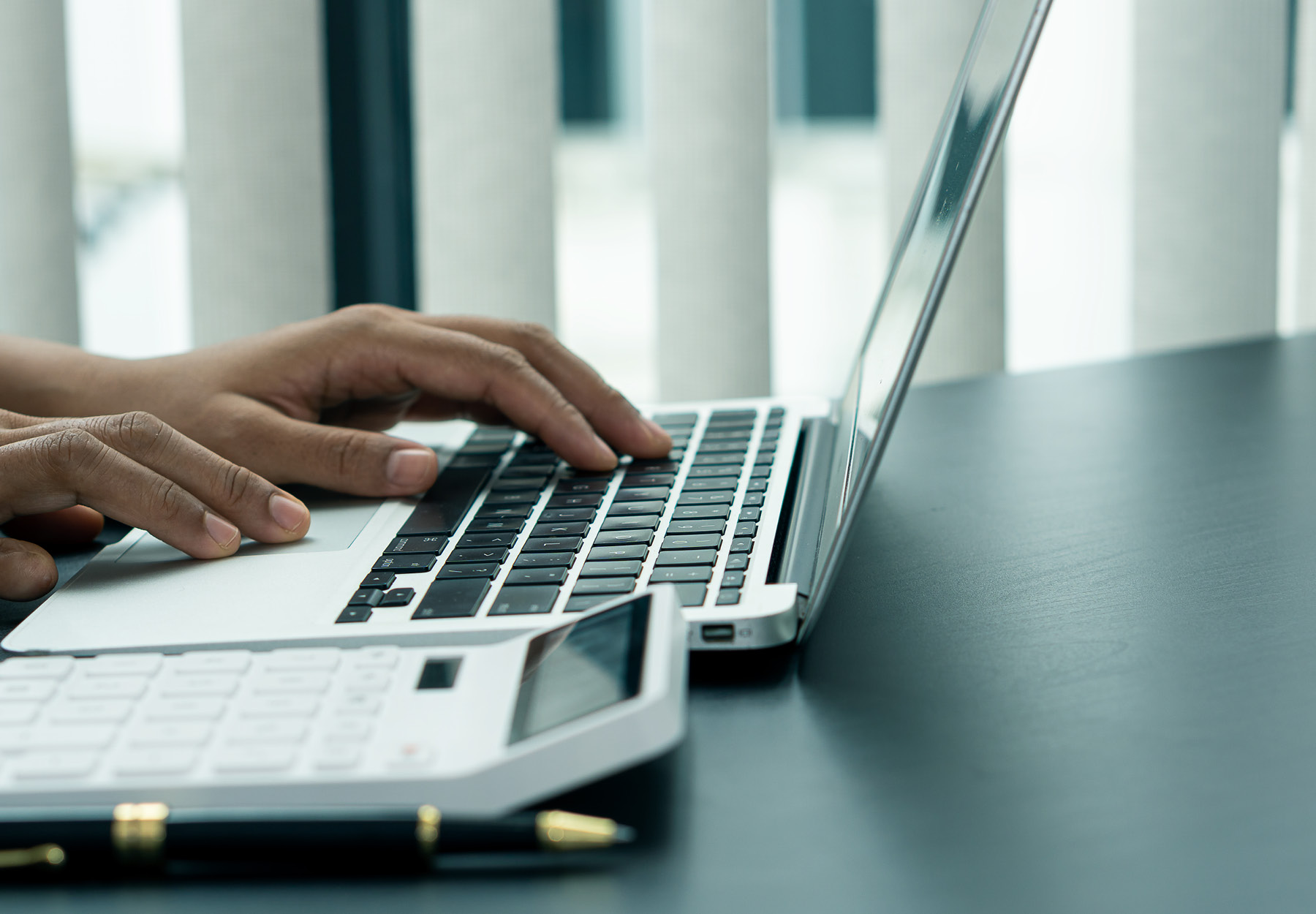 A closeup of someone typing with a calculator nearby.