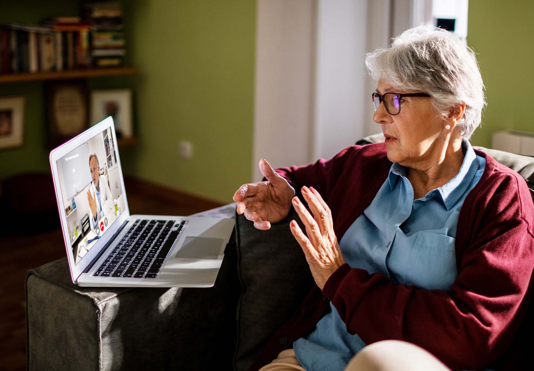 An elderly woman meets with her doctor via video conferencing on her laptop.