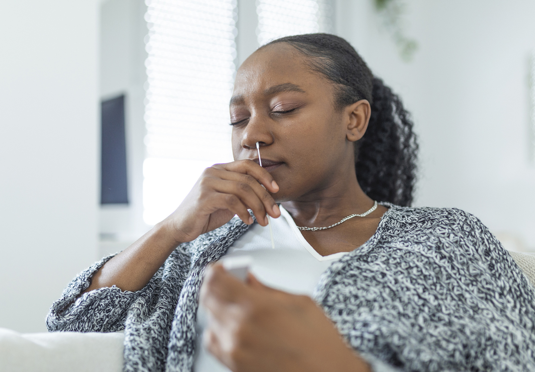Young Black woman at home using a nasal swab for COVID-19.