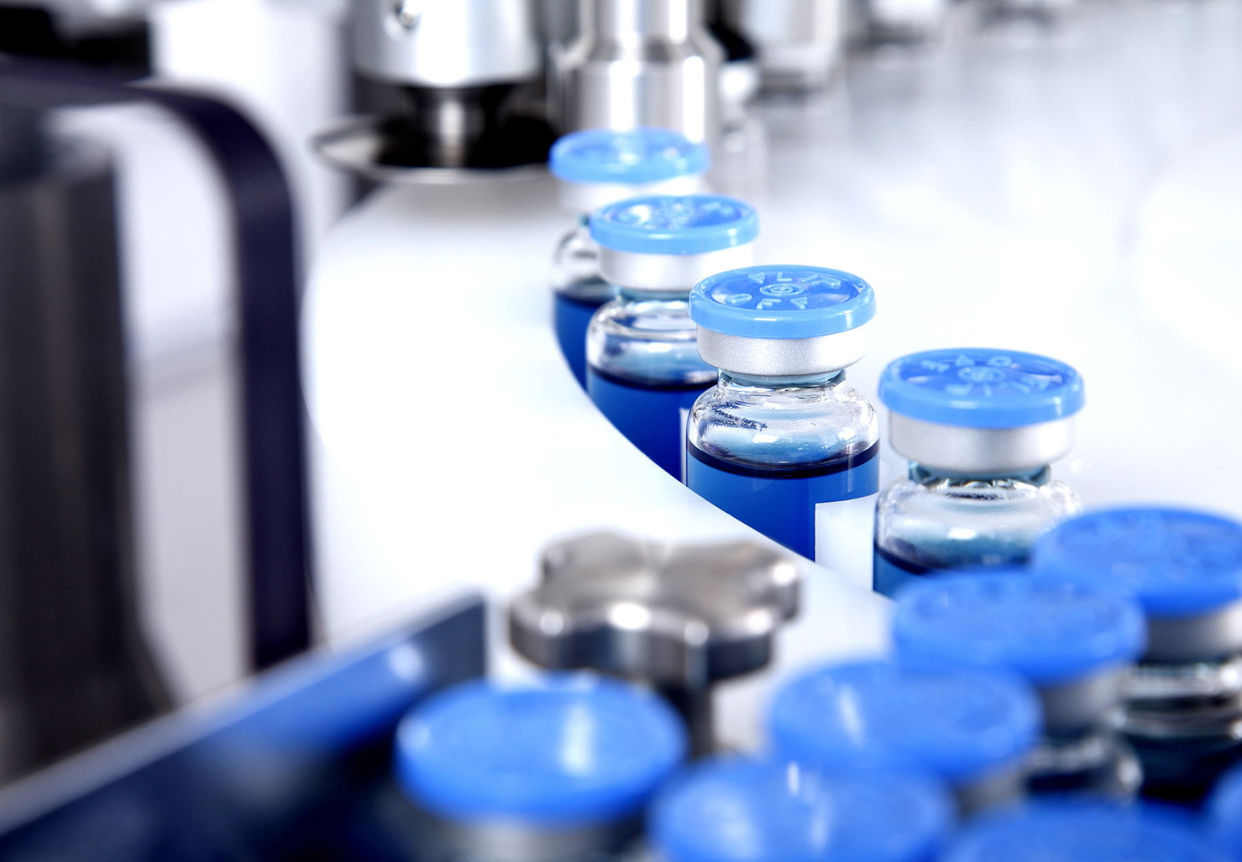 Glass bottles in production in the tray of an automatic liquid dispenser on the line in a pharmaceutical manufacturing plant.