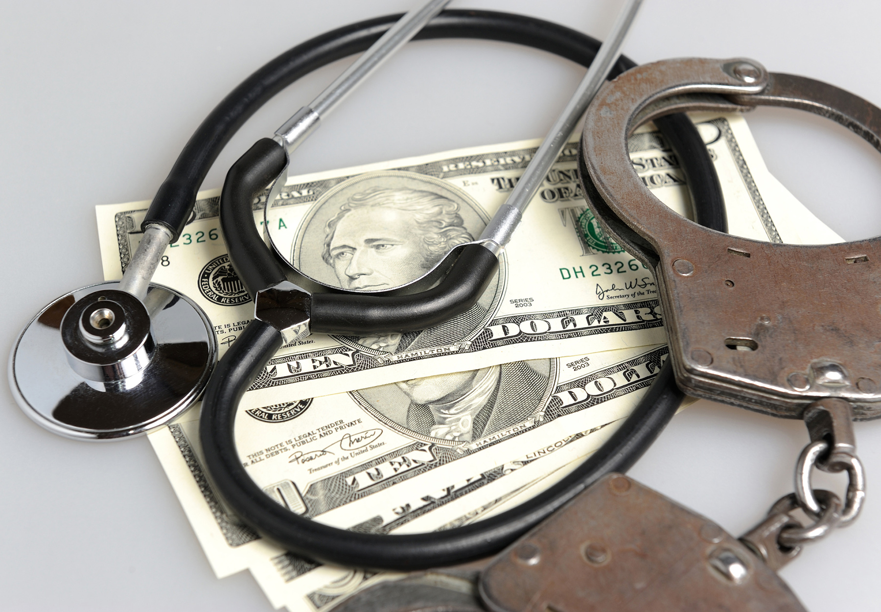 Stethoscope, handcuffs and money on gray background