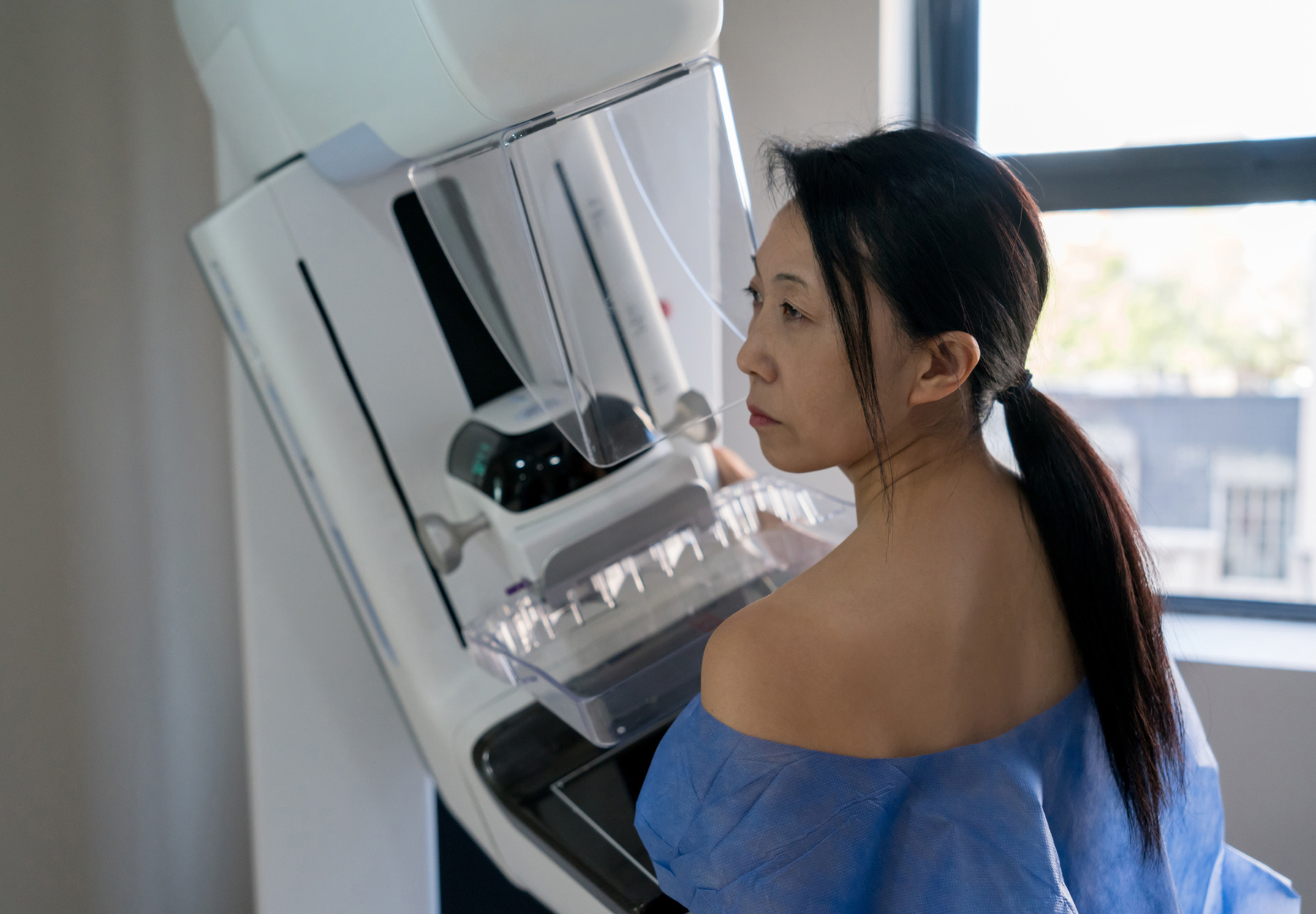 Asian female patient at the hospital getting a mammogram exam using a hospital gown and looking very serious