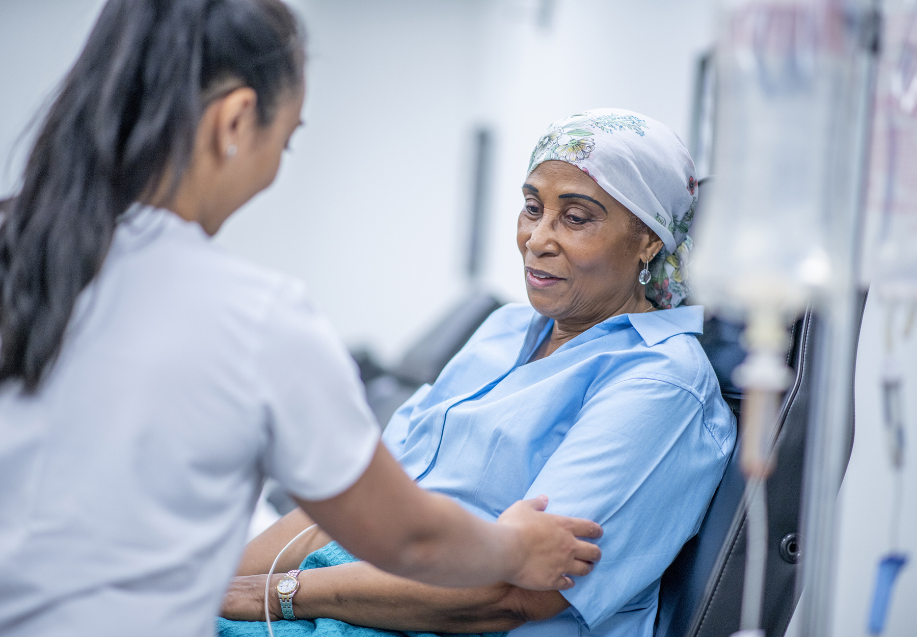 A woman wearing a head scarf recovers from chemo treatment in the hospital. A doctor speaks with her and offers her support.