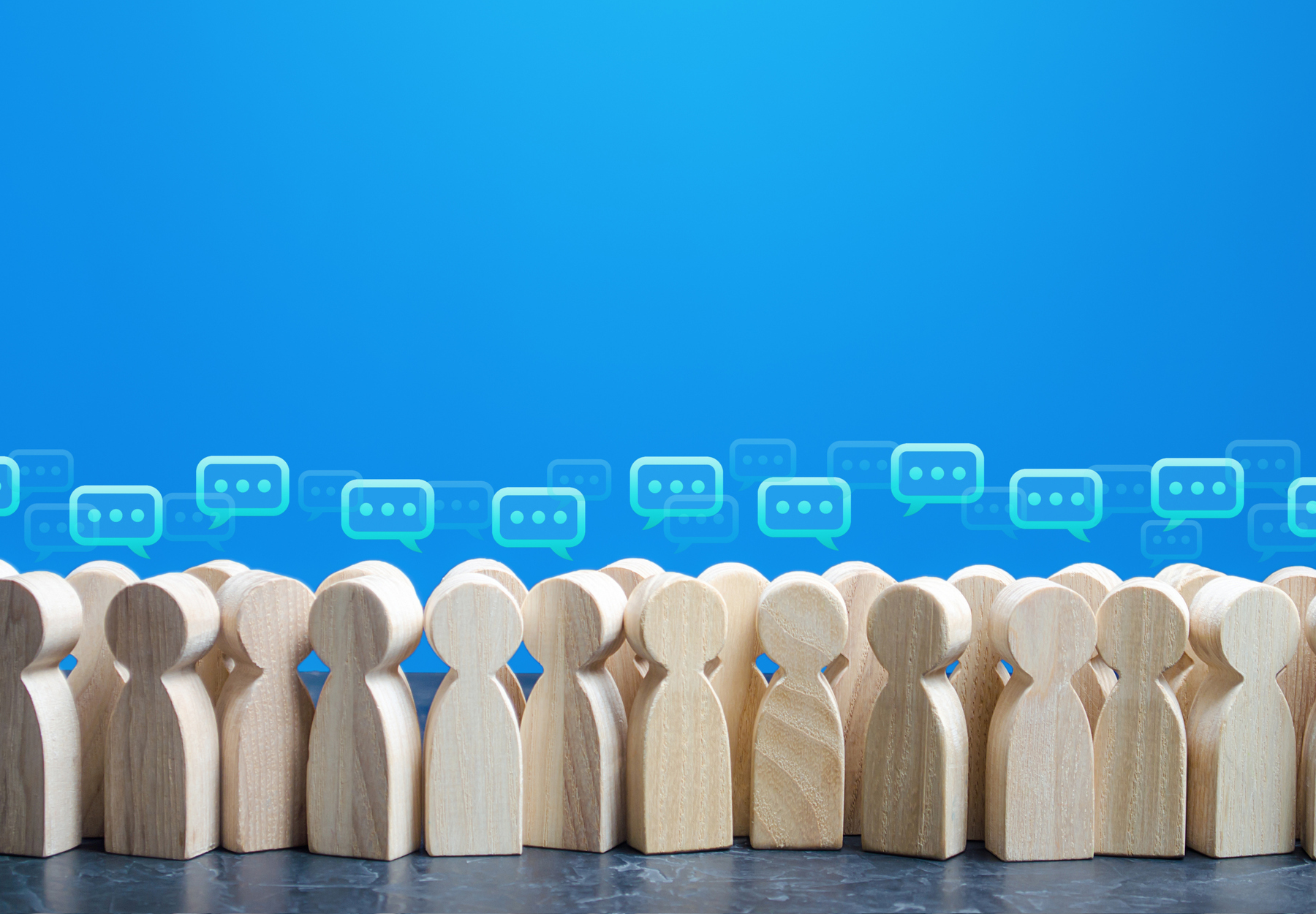 Wooden people markers stand in front of a blue background with word bubbles over their heads to show the concept of feedback.