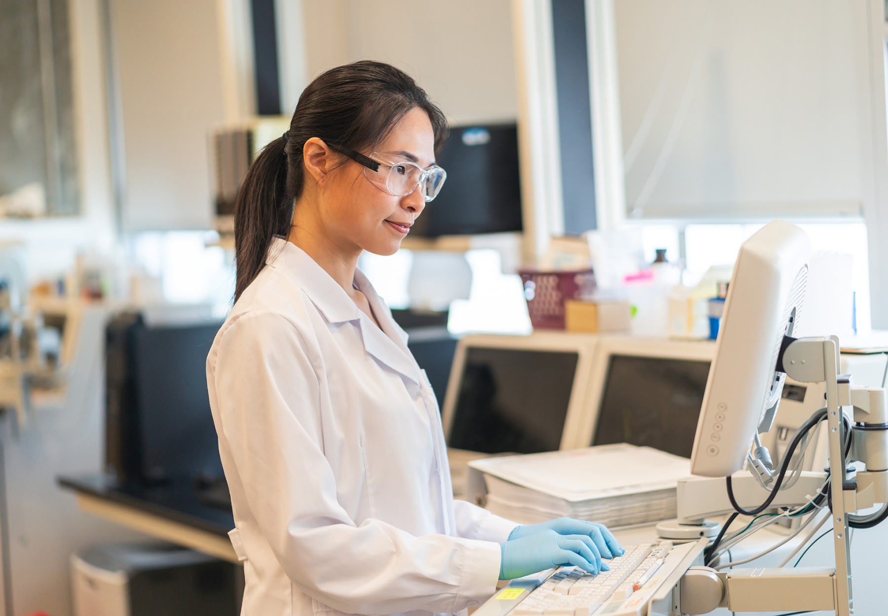 A female chemist of Chinese descent is working in a scientific lab. She is using a chemistry analyzer. The scientist is reviewing the results from the machine.