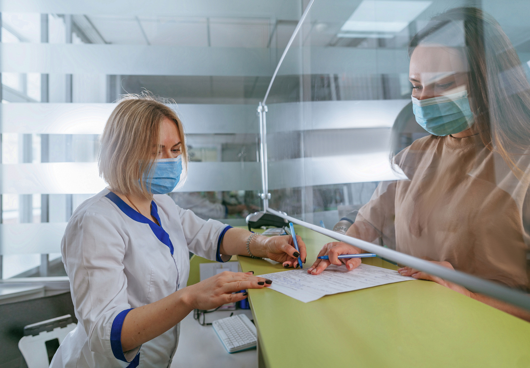 Female doctor or nurse explaining patient how to fill medical form at hospital reception