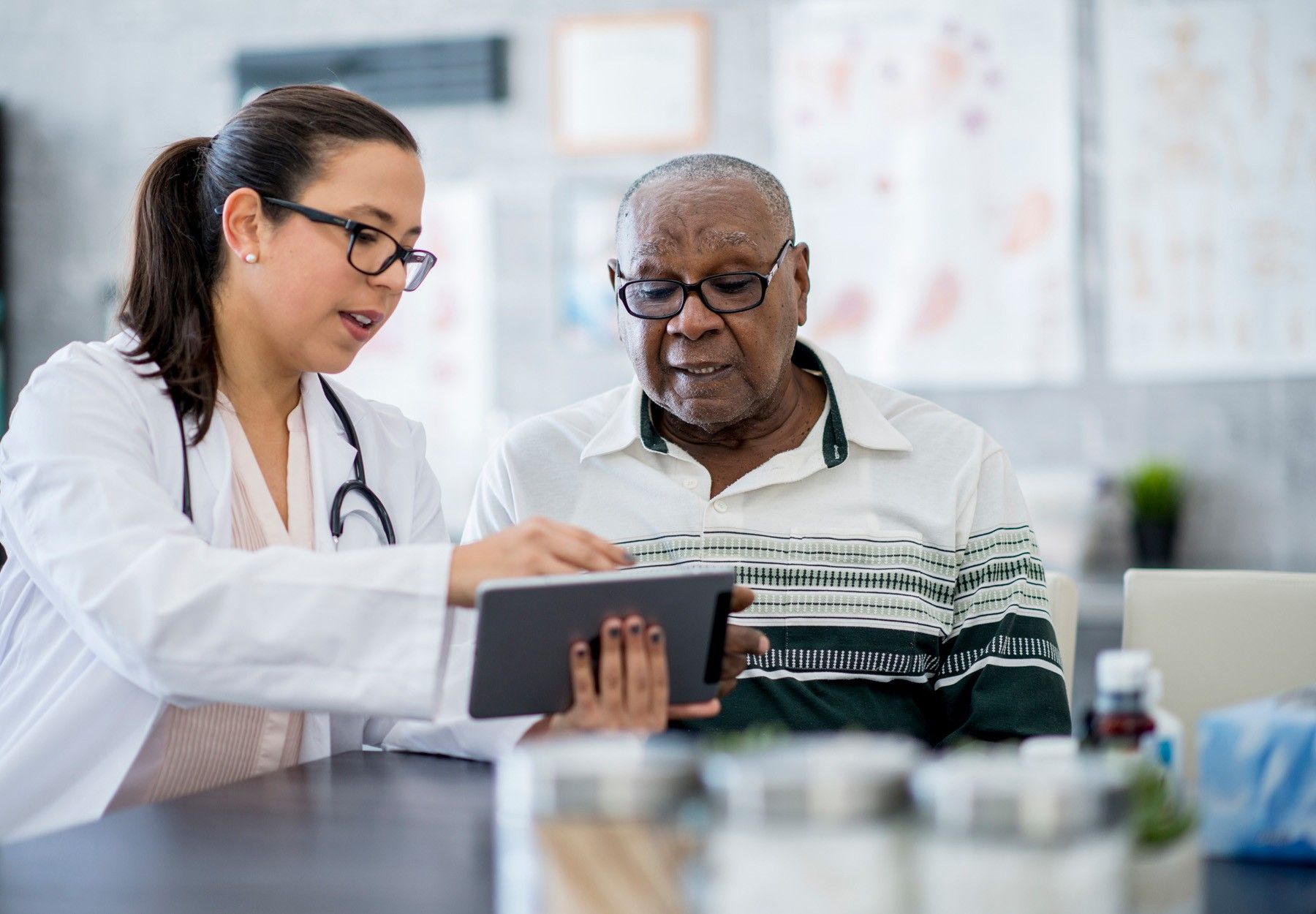A White doctor shares something on a tablet with an elderly Black patient