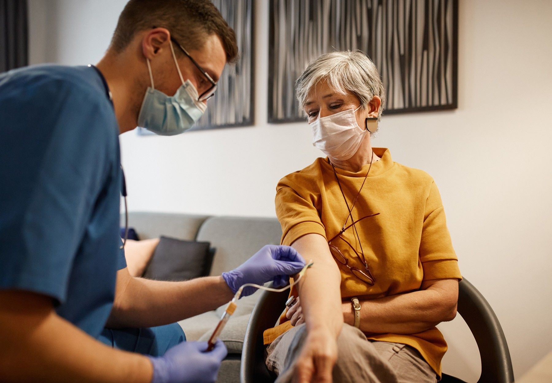 A health care worker takes a blood draw from a middle-aged woman in a yellow shirt