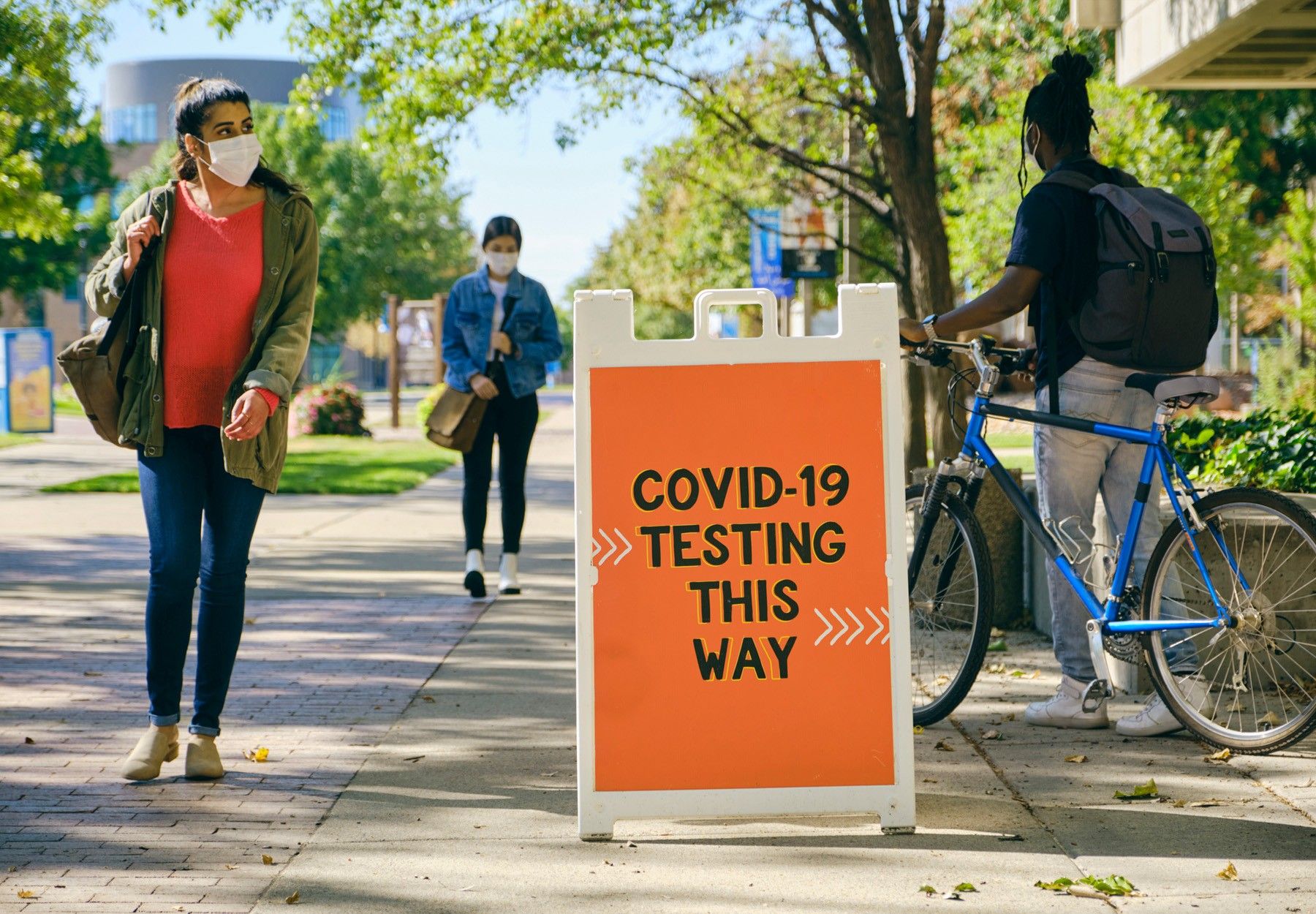 Masked people walk past an orange sign reading 