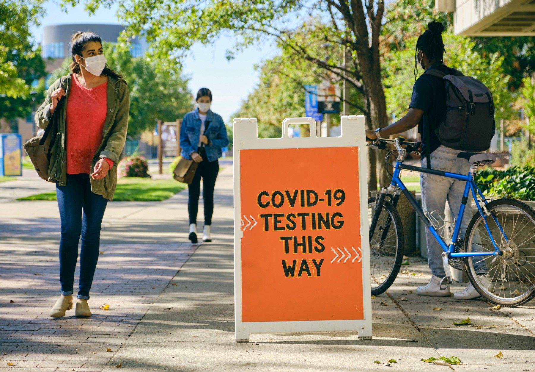 Masked people walk past an orange sign reading