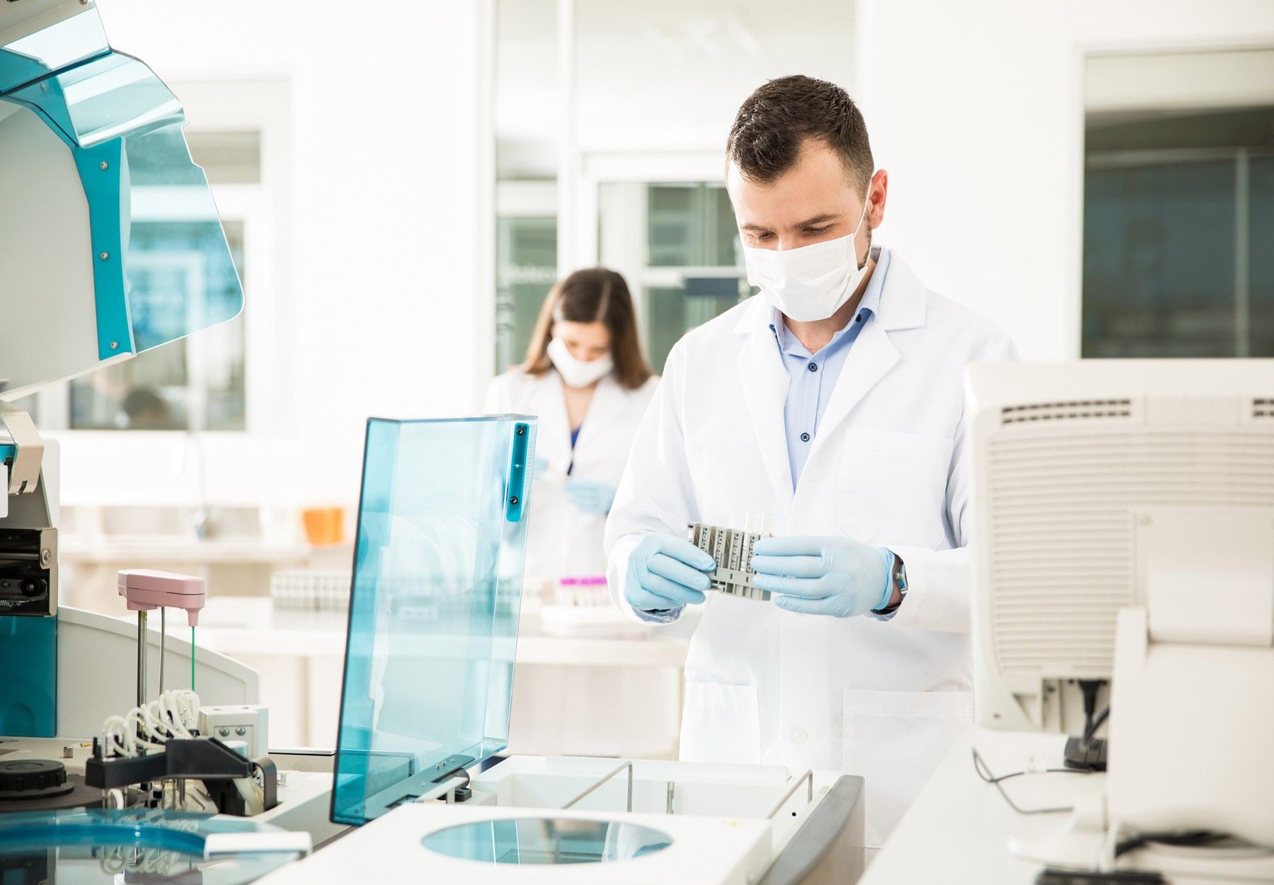 A male worker using an instrument in the lab with a female worker in the background stock image