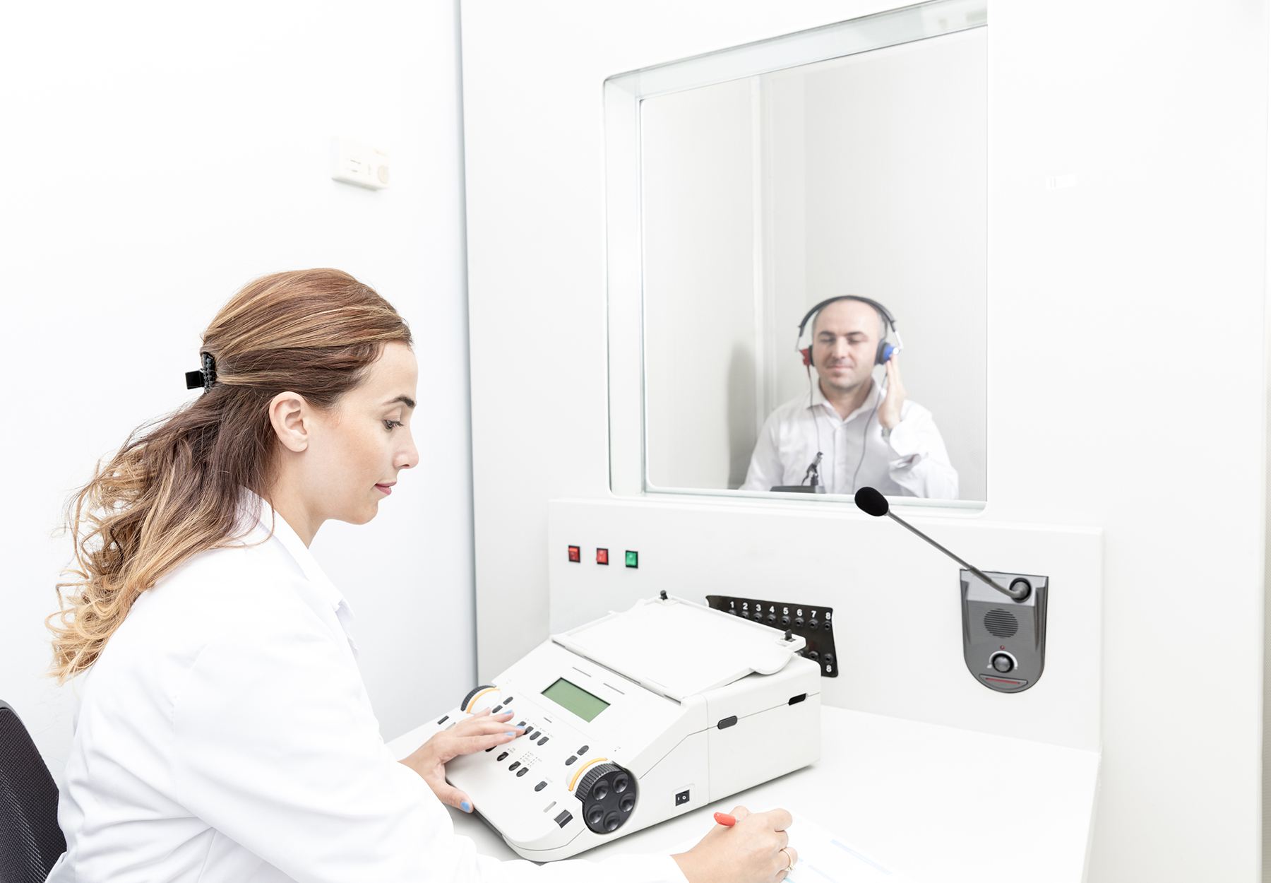 A female technician performs a hearing test on a male patient