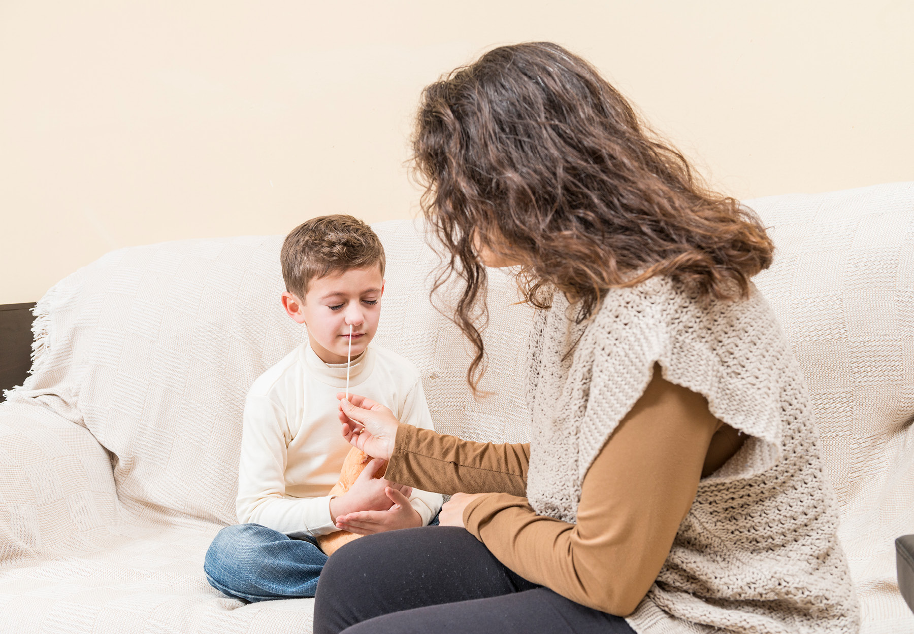 Stock image of a child receiving a nasal swab from his mother for an at-home COVID-19 test