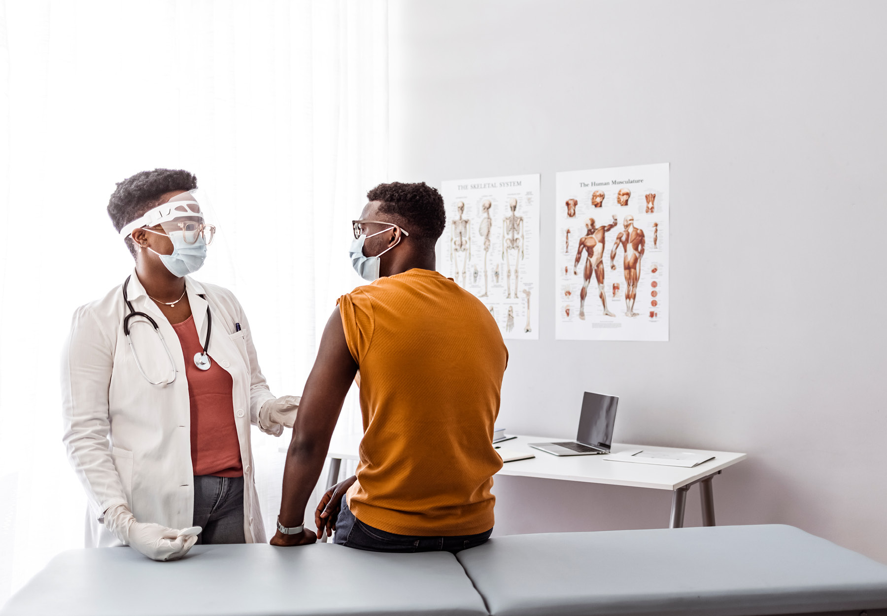 Patient sitting on a medical exam table is being examined by a physician