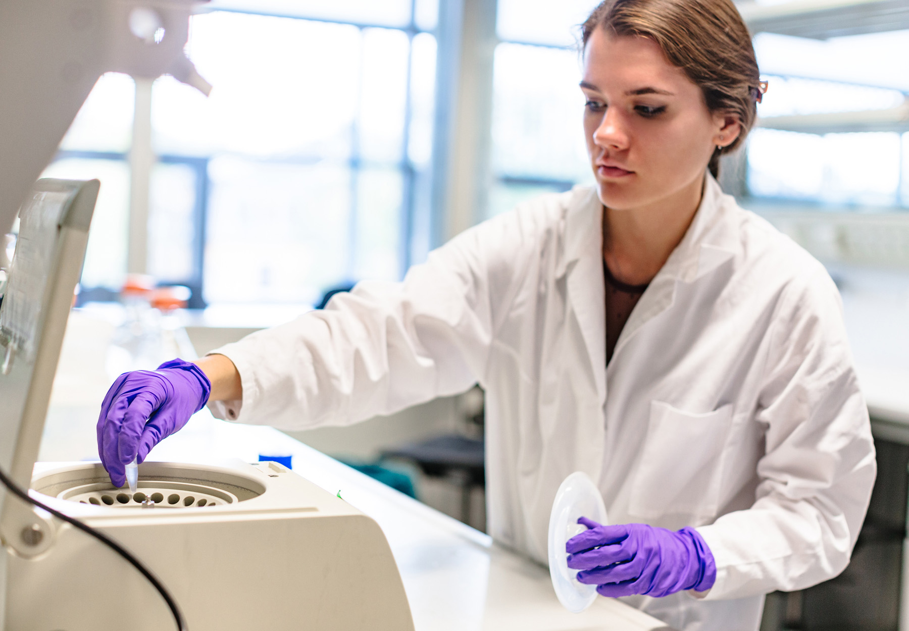 A female lab worker places a sample into a centrifuge in the lab in this stock photo