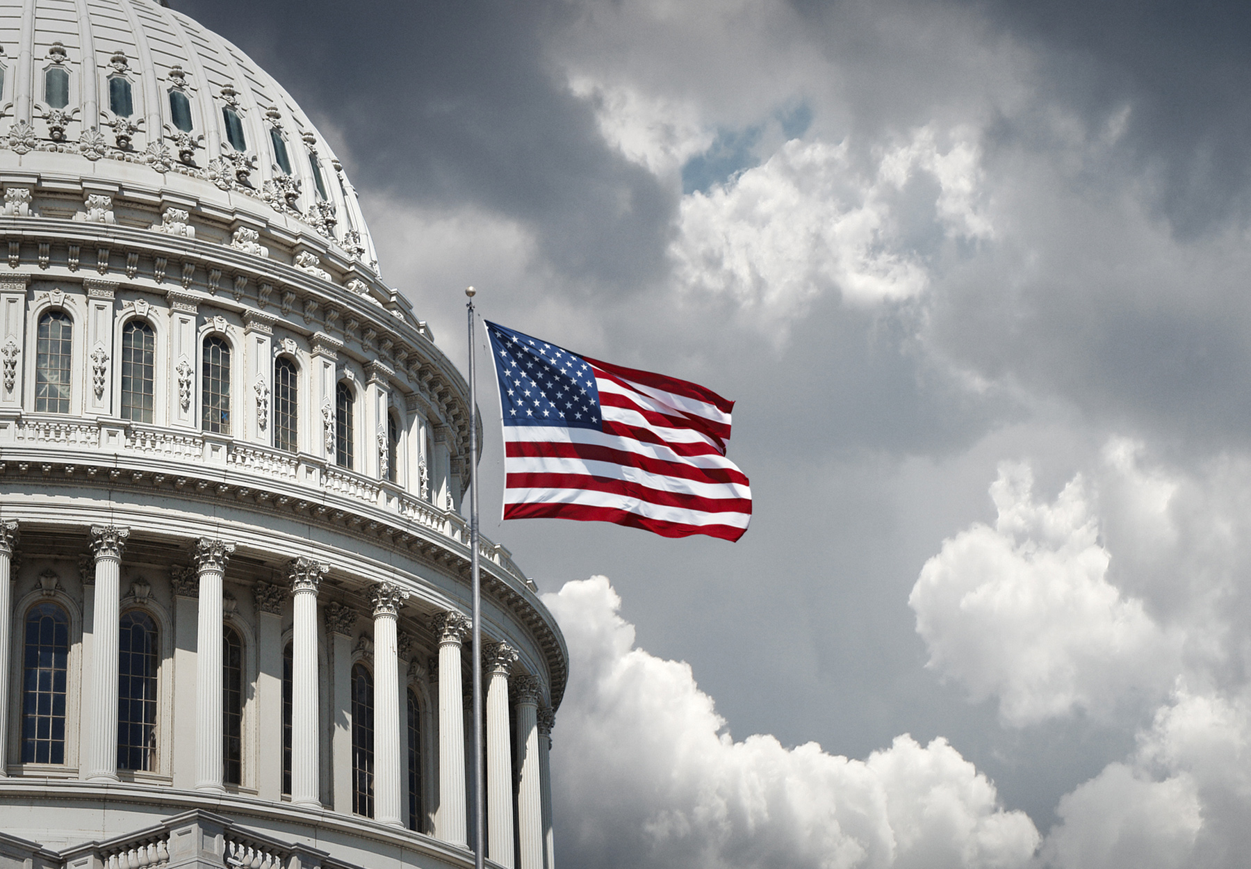 US Capitol and waving American flag beneath a cloudy sky. Stock image.