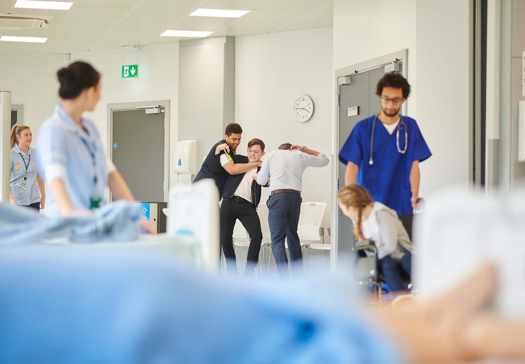 Two men restrain another man who is trying to get to health care workers in a hospital stock photo