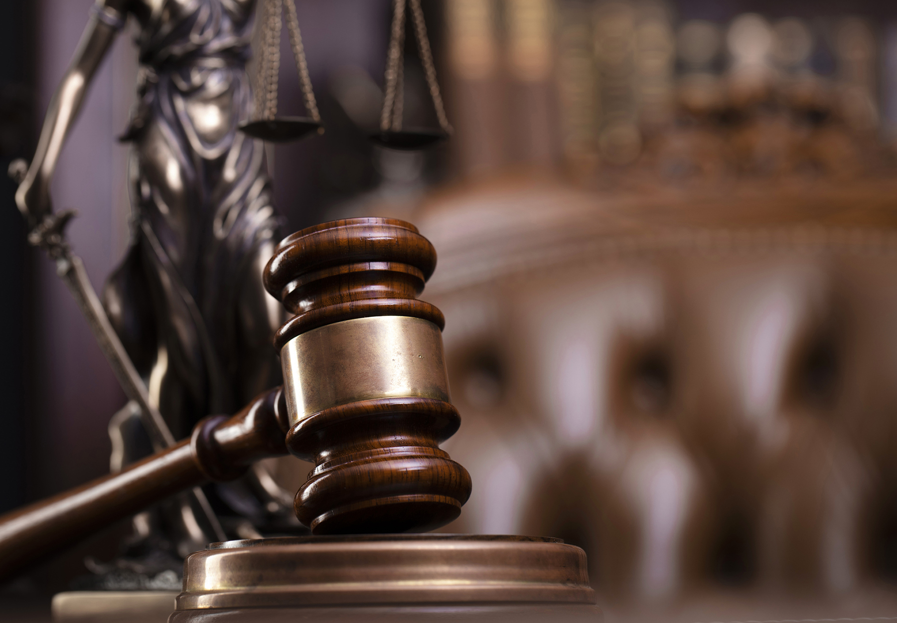 Stock image of a judge’s gavel, Themis sculpture and collection of legal books on a brown background to show the concept of a court case..