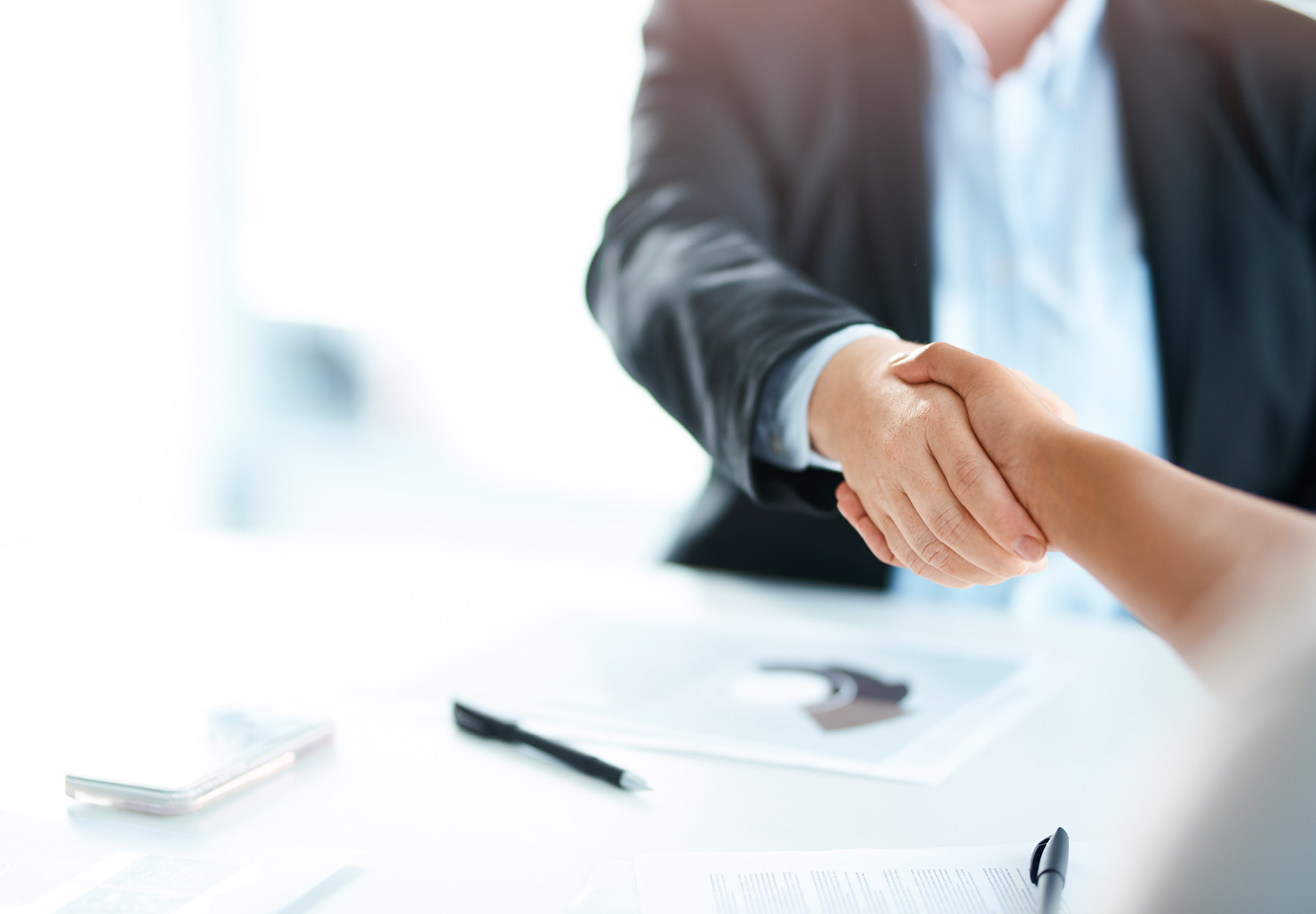 Cropped stock image of two businesswomen shaking hands during a meeting in a modern office