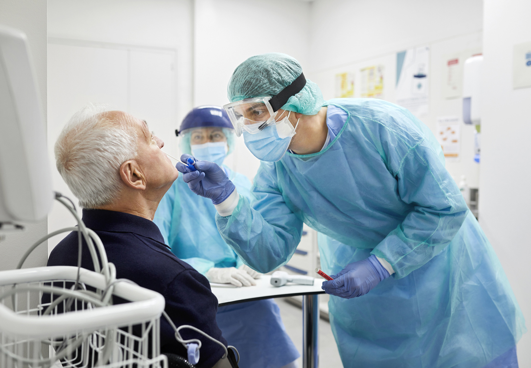 Doctor taking coronavirus sample from male patient's nose. Frontline worker is in protective workwear. They are at hospital. Stock photo.