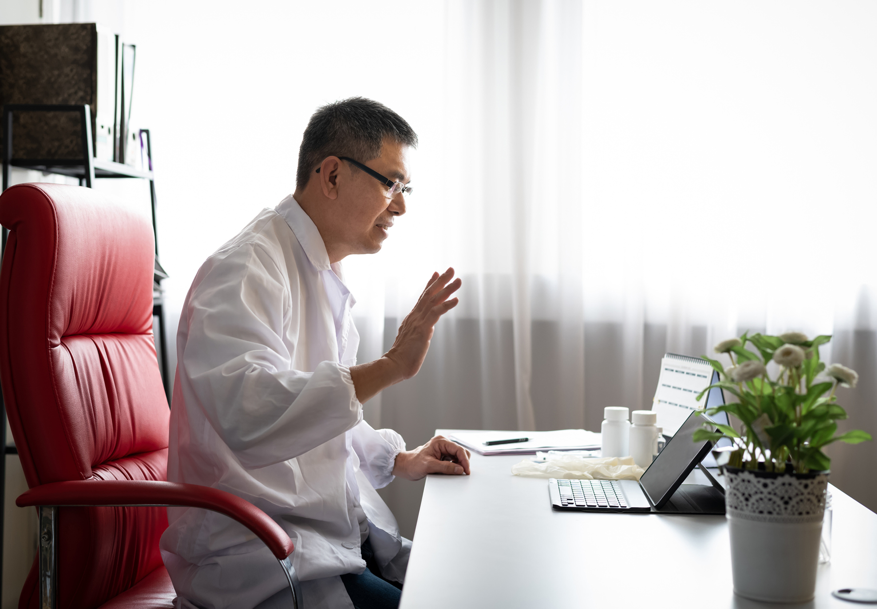 A lab professional waves at his tablet in a virtual meeting. Stock image.