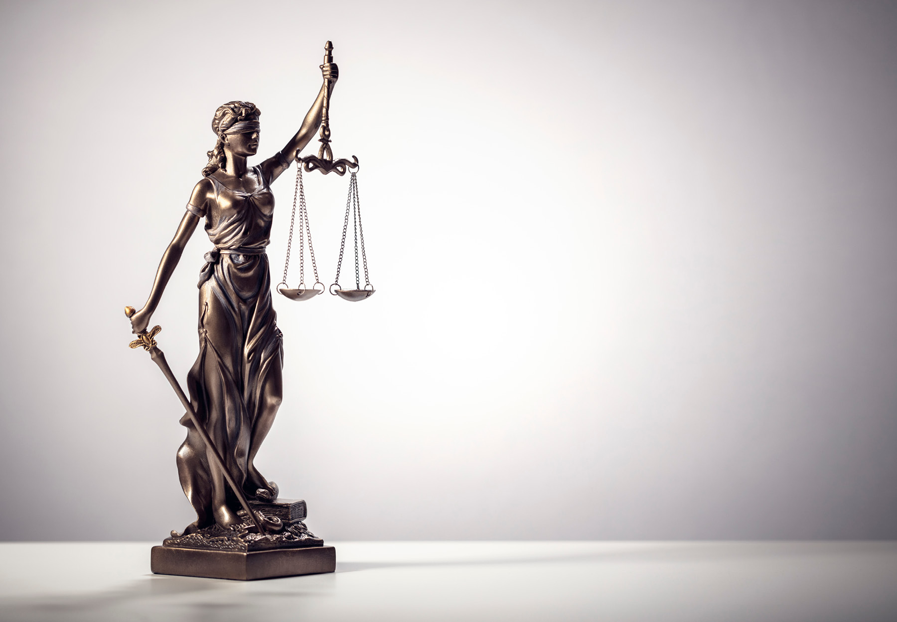 Stock image of a bronze blindfolded Lady Justice statue holding a sword and a set of scales