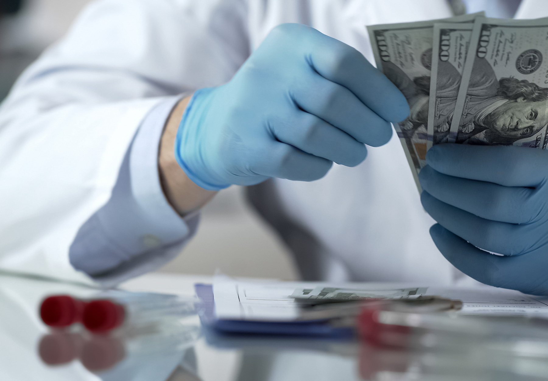 Closeup stock image of lab worker in PPE holding a stack of US money