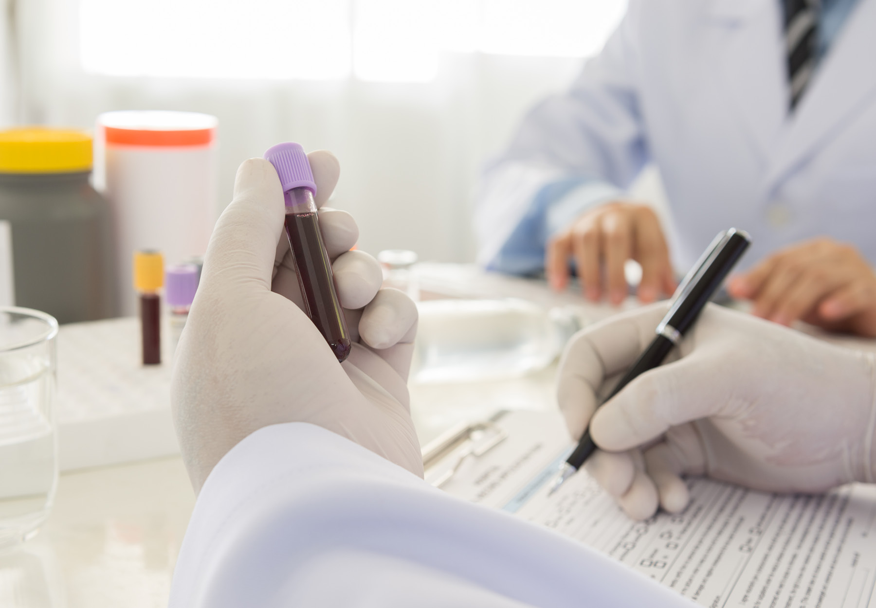 Closeup stock image of lab worker holding a blood sample tube in one hand and filling out a form with the other hand