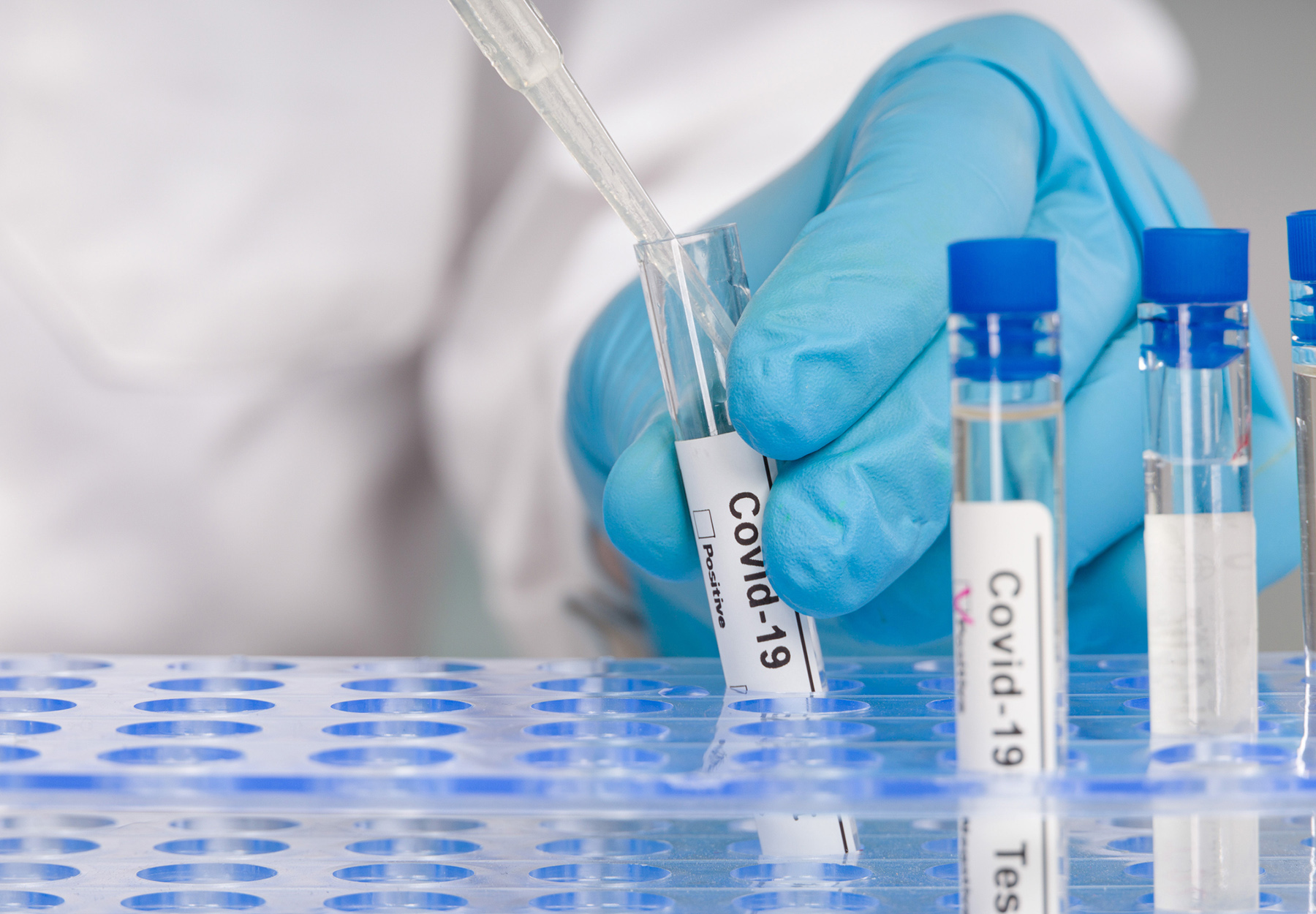 Closeup stock photo of lab worker in PPE working with test tubes labeled 
