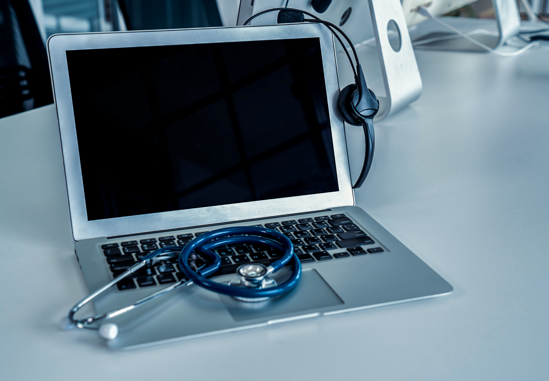 Stock image of headset and stethoscope at clinic ready for online video call with patient. Concept of telehealth and telemedicine service.