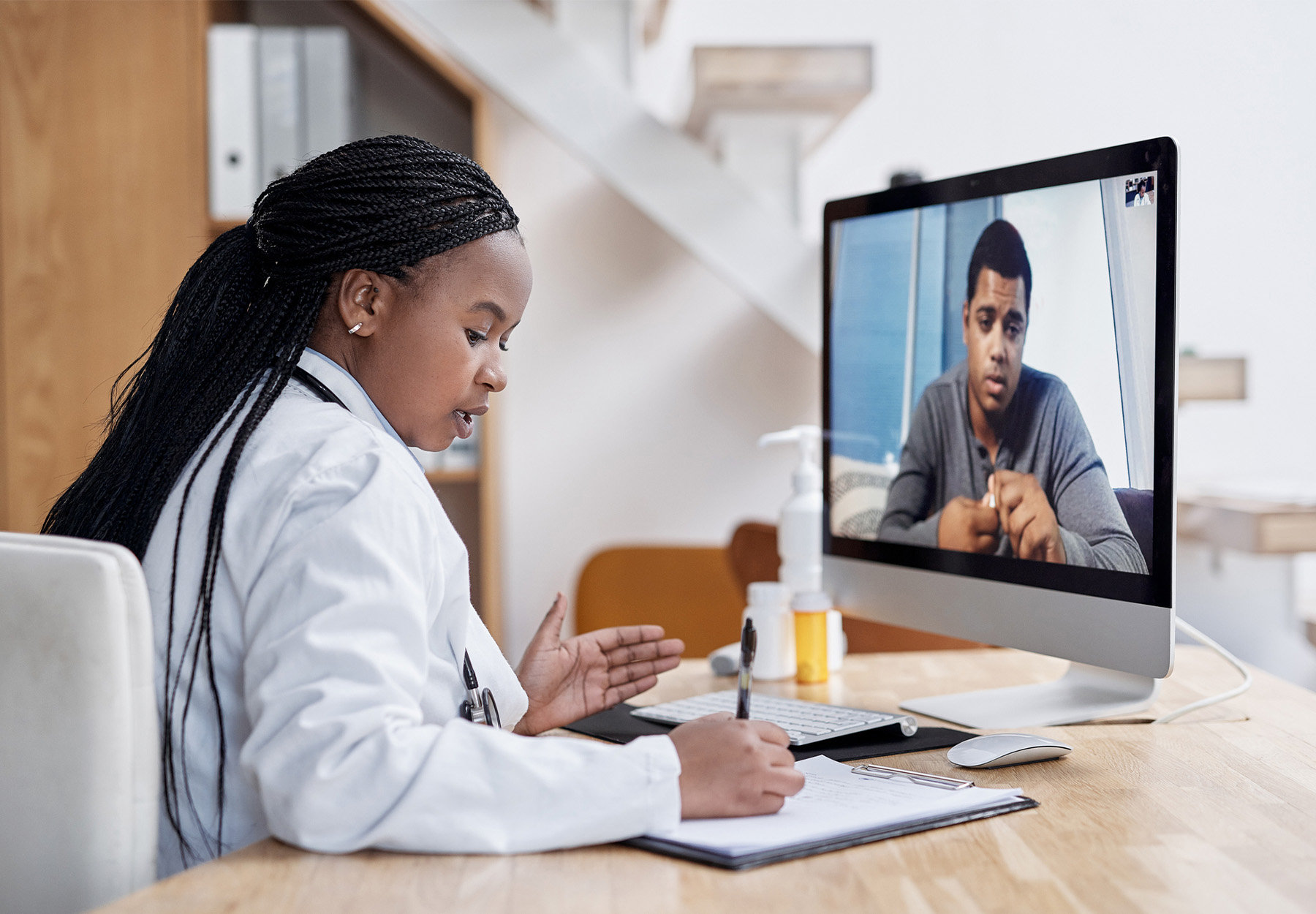 Stock photo of a young doctor writing notes during a video call with a patient on a computer