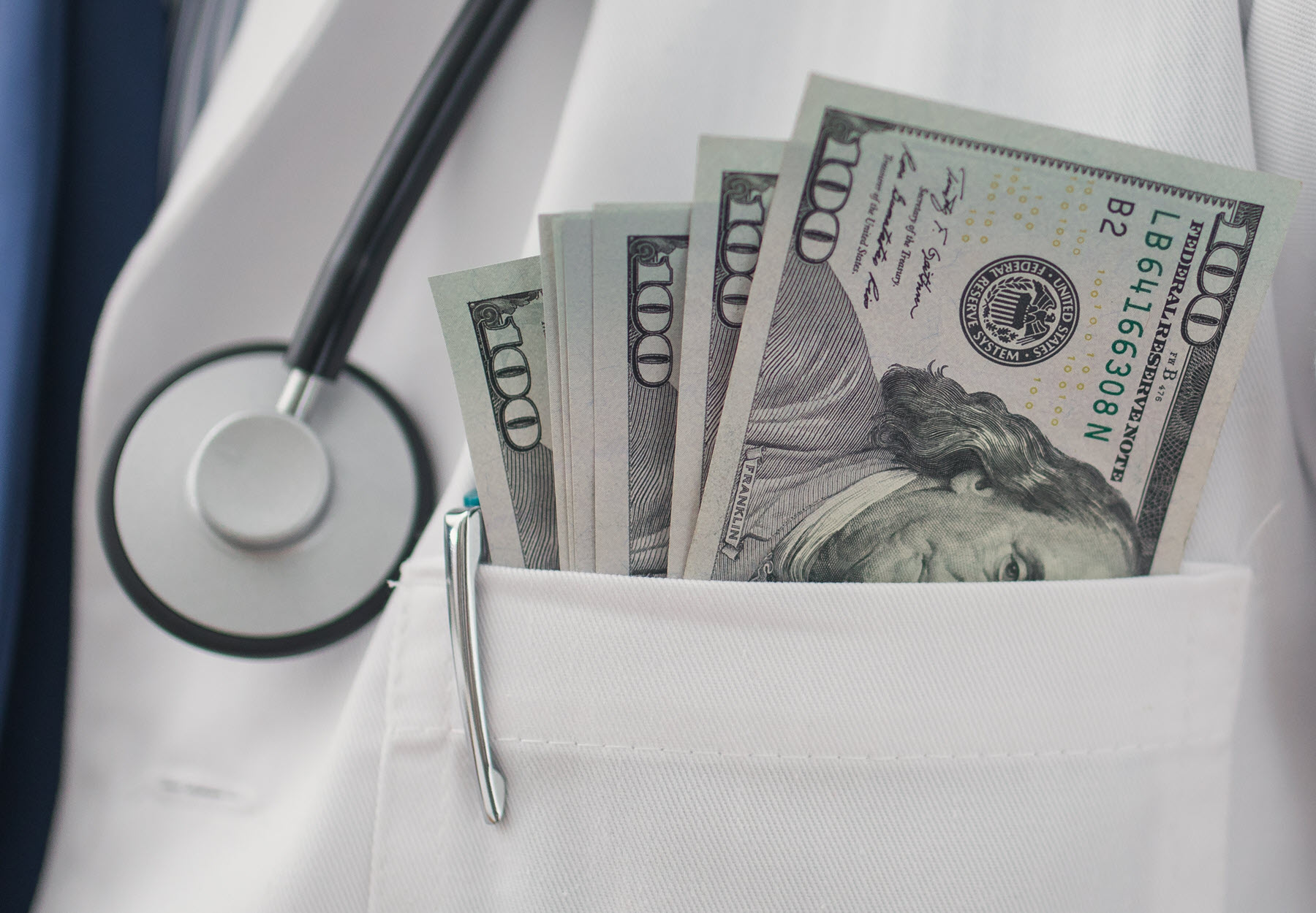 Closeup of doctor's coat pocket with US cash inside to represent kickbacks concept. Stock image.