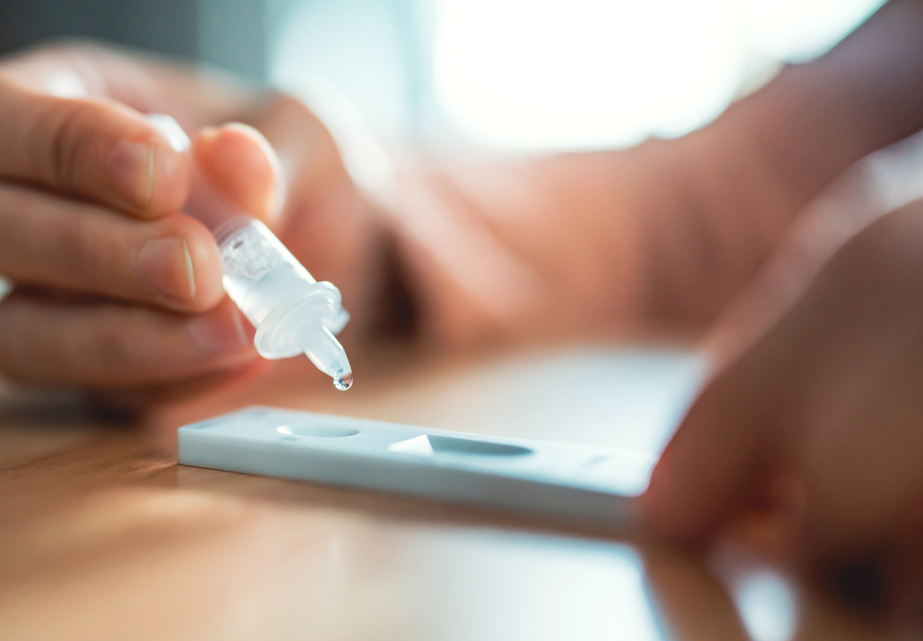 Close up of woman dropping fluid from nasal swab with dropper onto COVID-19 Rapid Antigen Test cartridge. Stock photo.