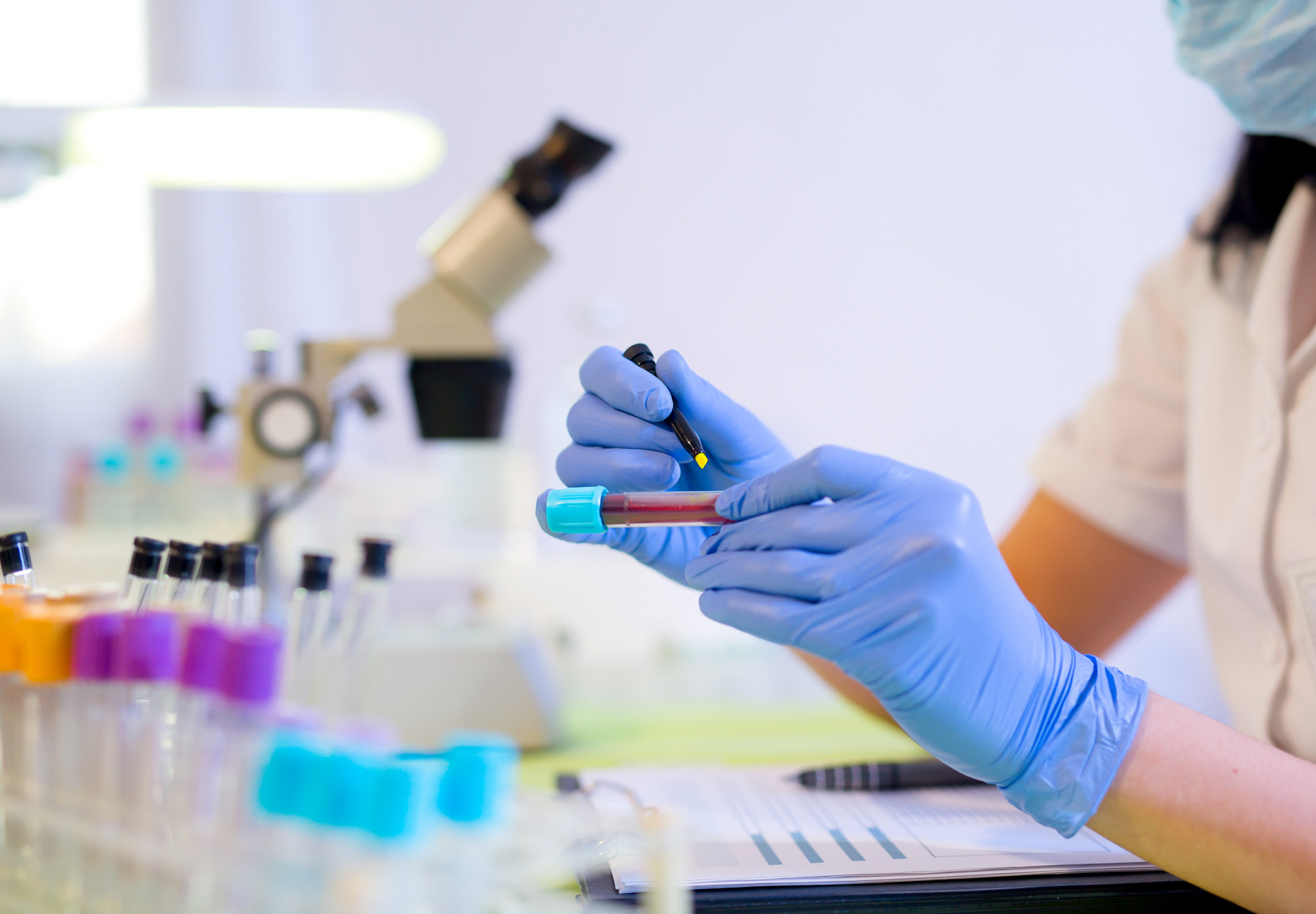 Woman working in a laboratory. She writes with a felt pen on a blood sample tube. Stock photo.