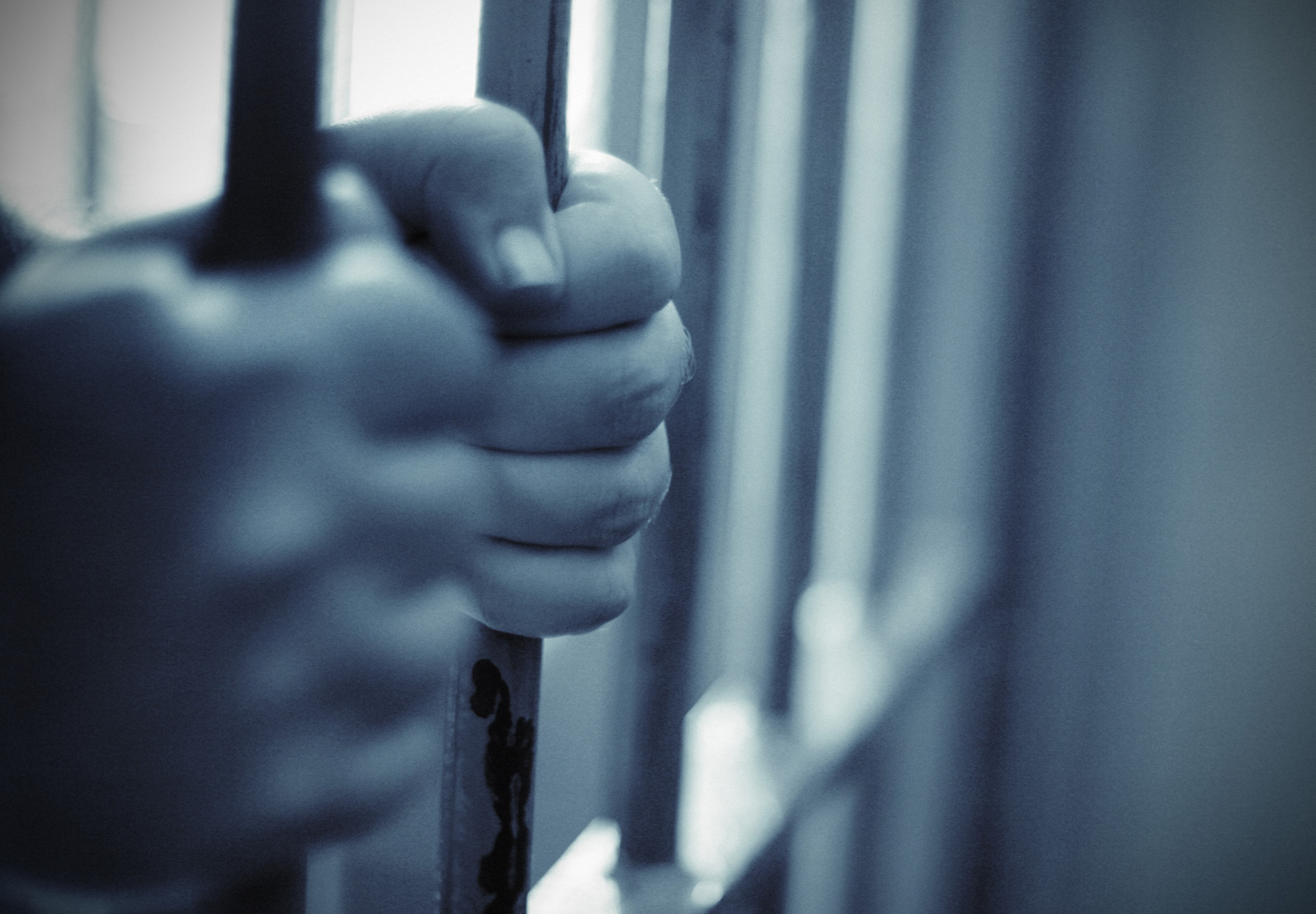 A black and white photo of hands gripping the bars of a prison cell. Stock image.