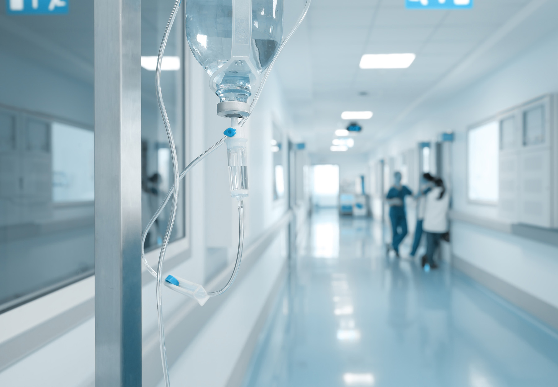 Hospital hallway with IV in the foreground and a group of staff meeting in the background. Stock image.