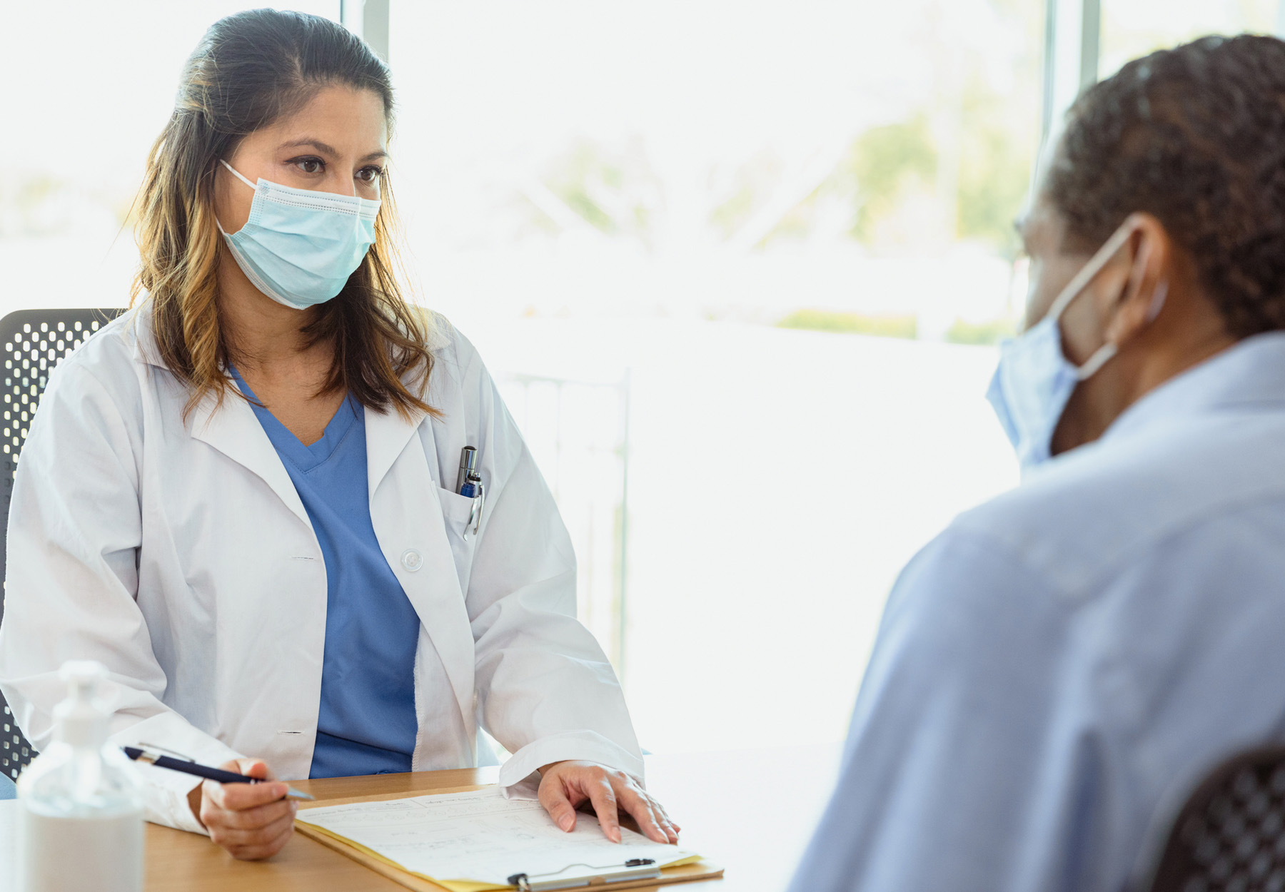 Healthcare professional filling a form out with a patient at a desk.