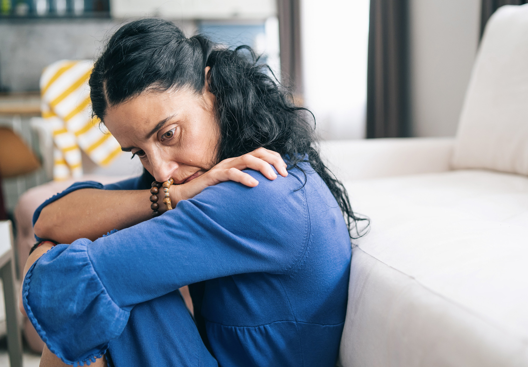 Depressed woman wearing blue sits slumped on her floor. Stock photo.