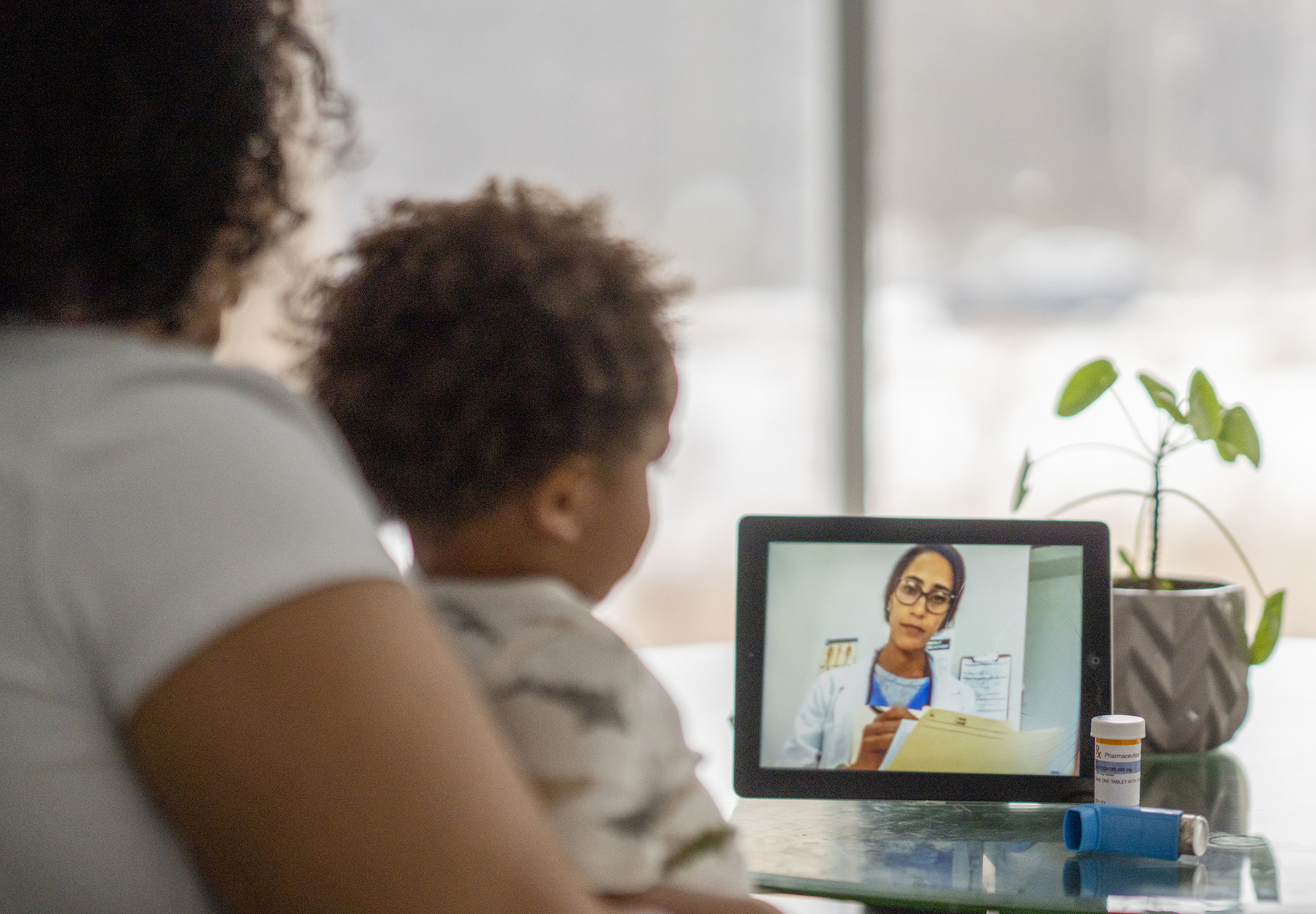 African American mother sitting with her sick child and speaking with a medical professional via video chat during the COVID-19 pandemic. Stock photo.
