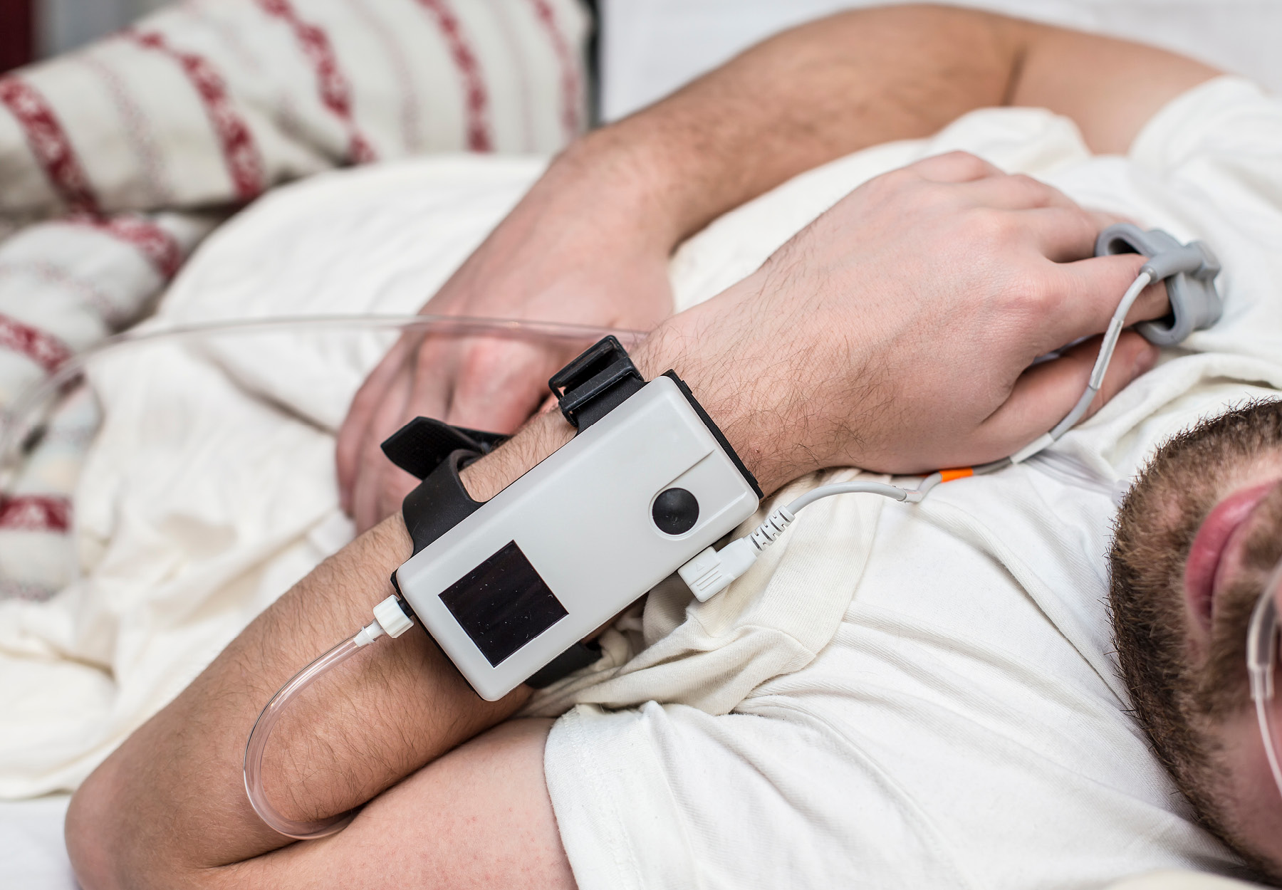 Closeup photo of man in bed who is wearing a sleep apnea monitor on his wrist. Stock photo.